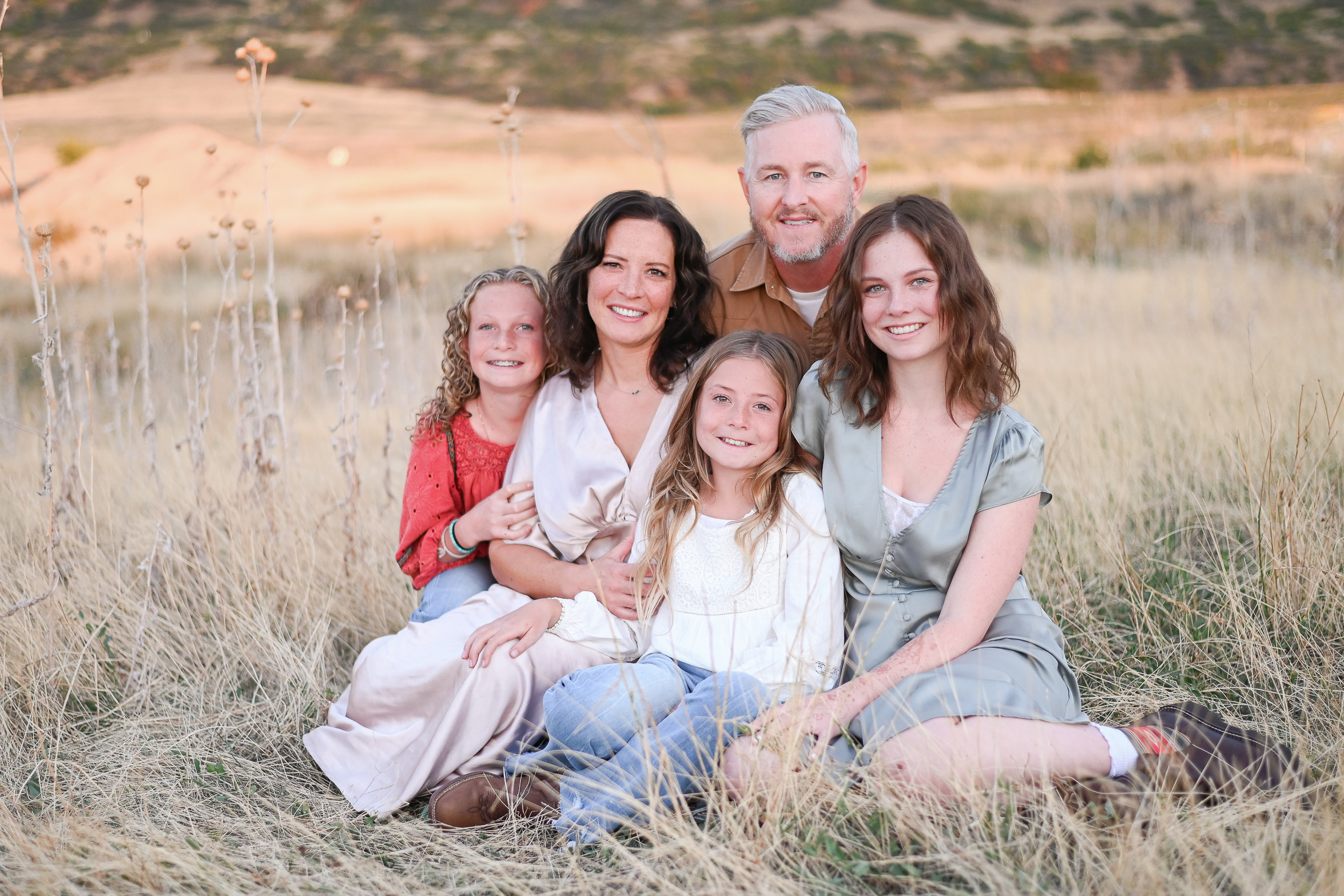 Family sitting in the tall grasses in the foothills of the mountains of Mapleton Utah.