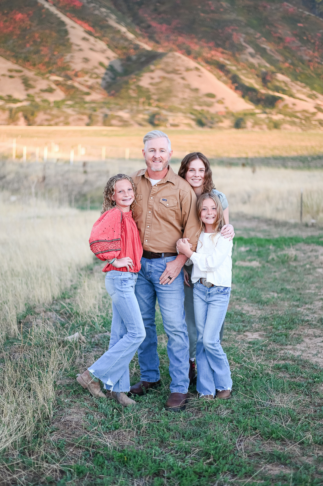 Dad smiles hand in hand with his daughters in the foothills of the mountains in Mapleton Utah.