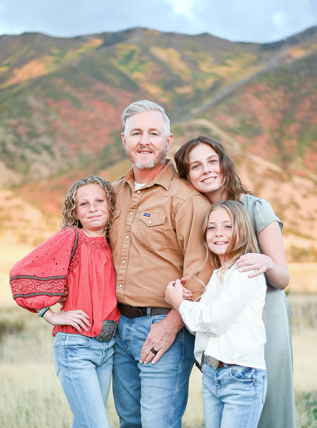 Dad smiles hand in hand with his daughters in the foothills of the mountains in Mapleton Utah.