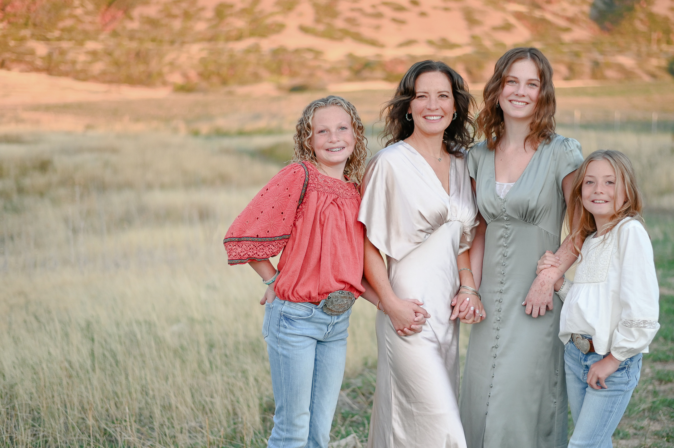 Mom smiles hand in hand with his daughters in the foothills of the mountains in Mapleton Utah.