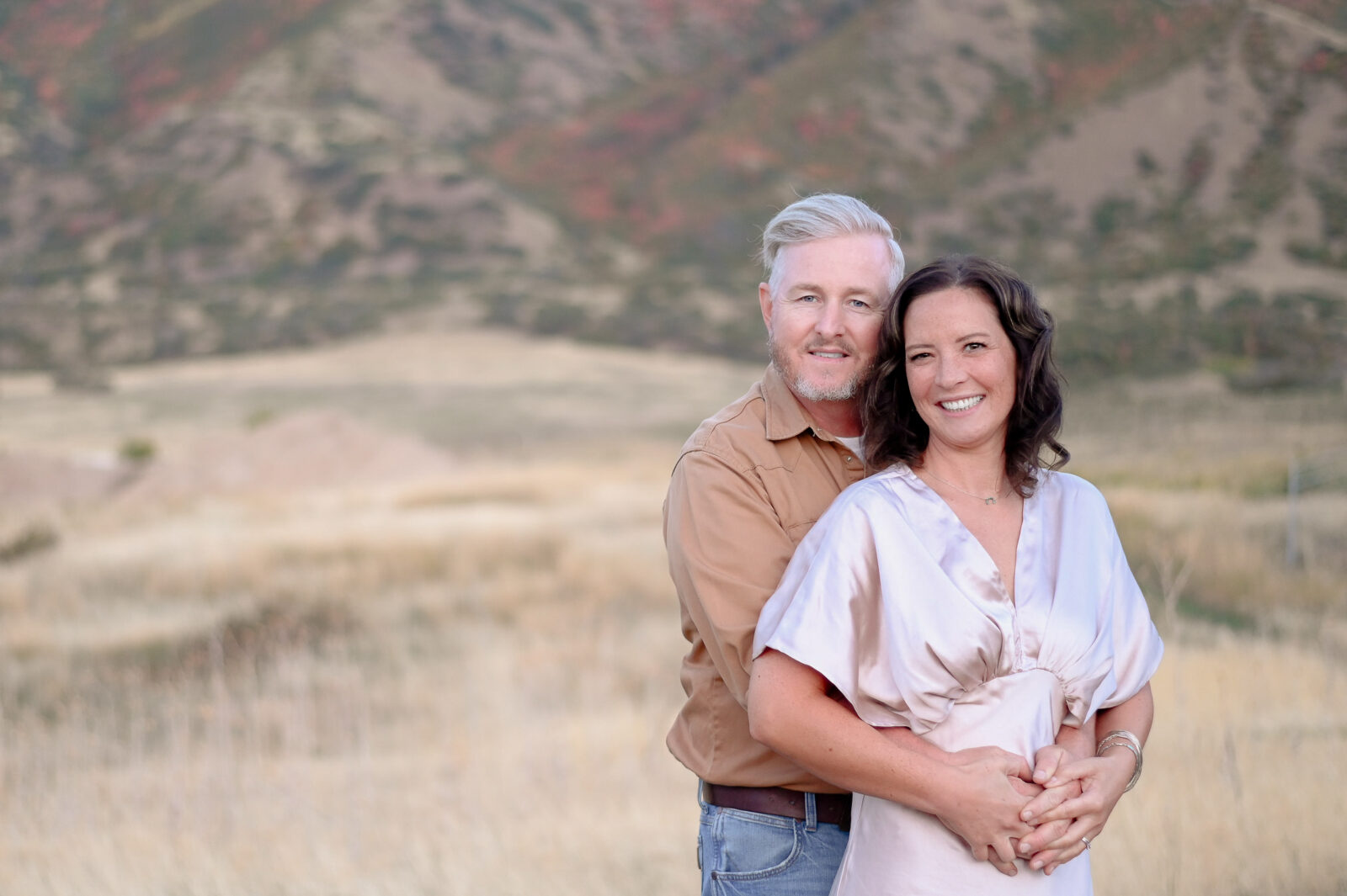 A couple embracing one anotherwith smiles on their faces in the foothills of the mountains in Mapleton Utah.