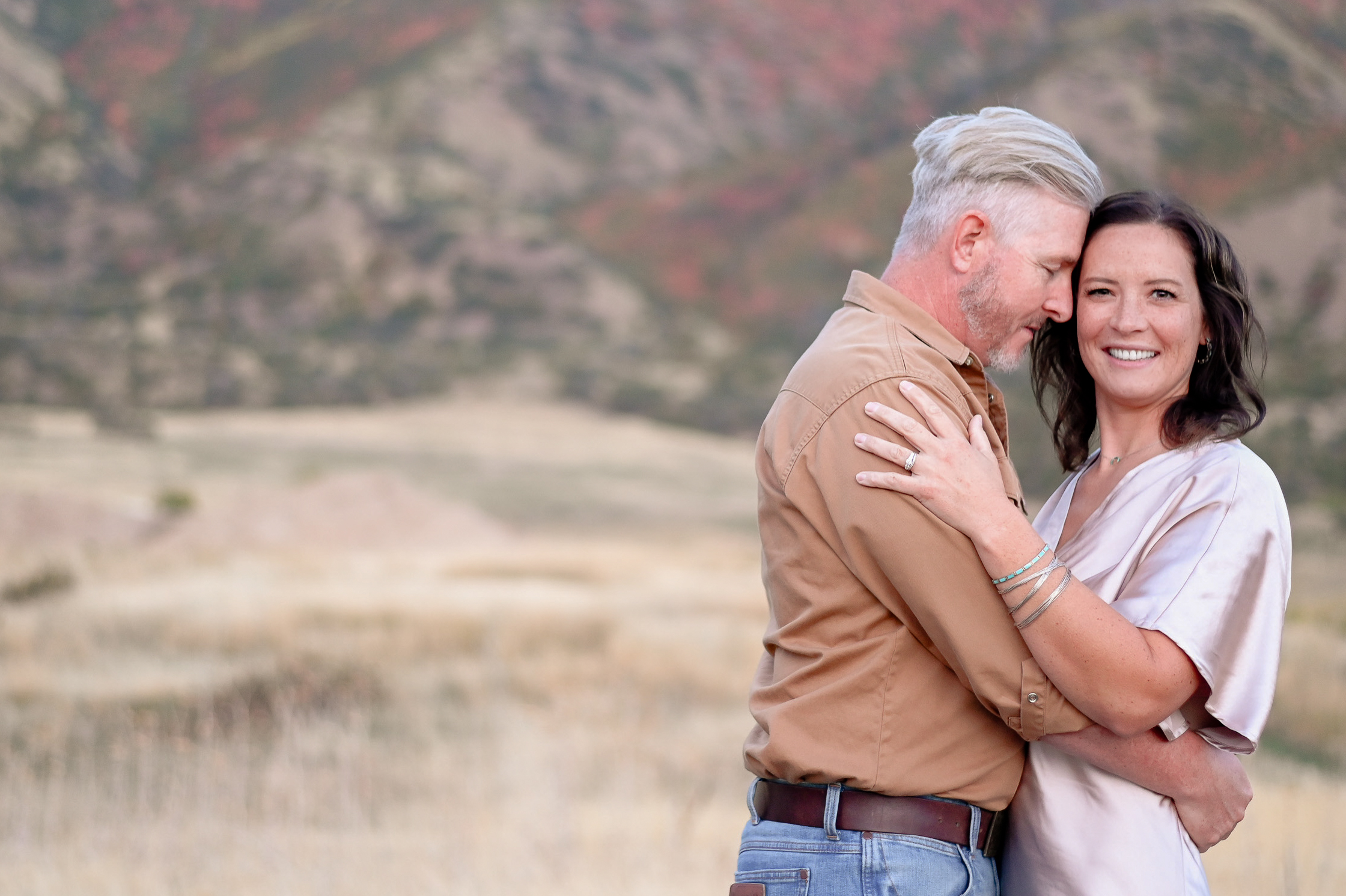 A couple embracing one anotherwith smiles on their faces in the foothills of the mountains in Mapleton Utah.