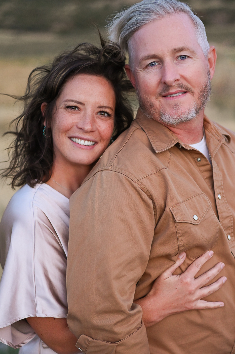A couple embracing one anotherwith smiles on their faces in the foothills of the mountains in Mapleton Utah.