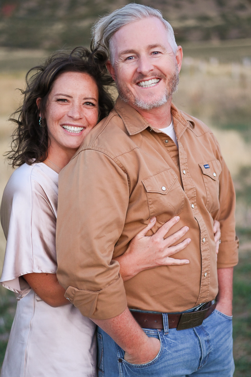 A couple embracing one anotherwith smiles on their faces in the foothills of the mountains in Mapleton Utah.