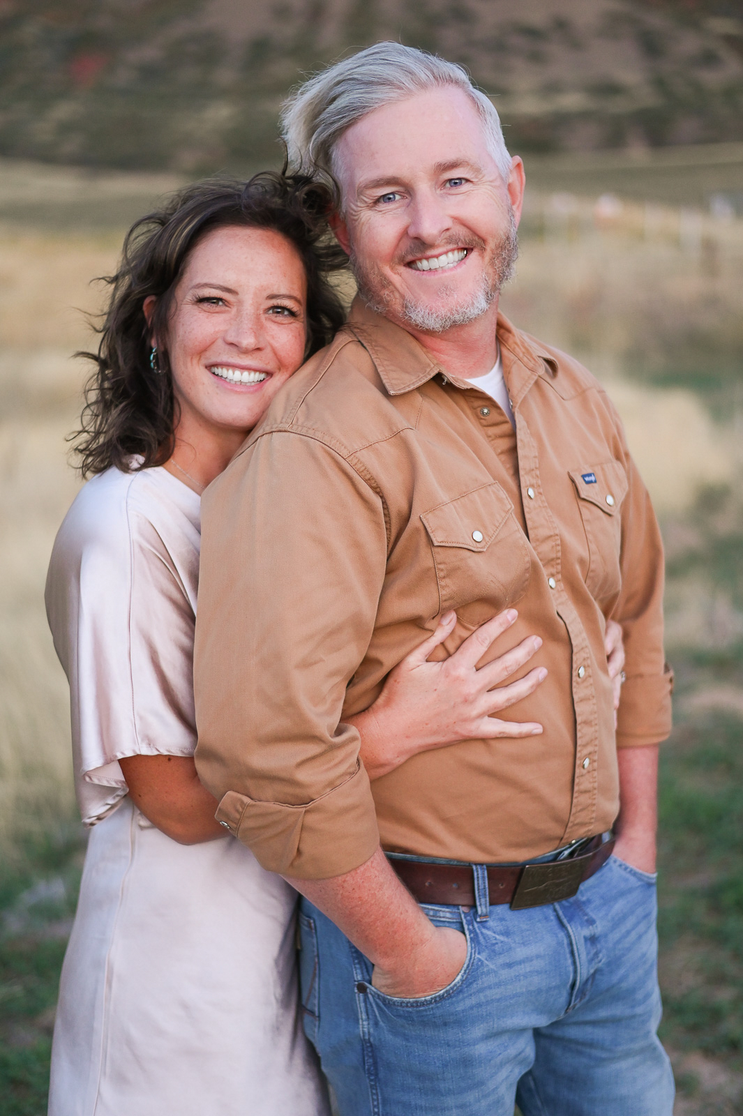 A couple embracing one anotherwith smiles on their faces in the foothills of the mountains in Mapleton Utah.
