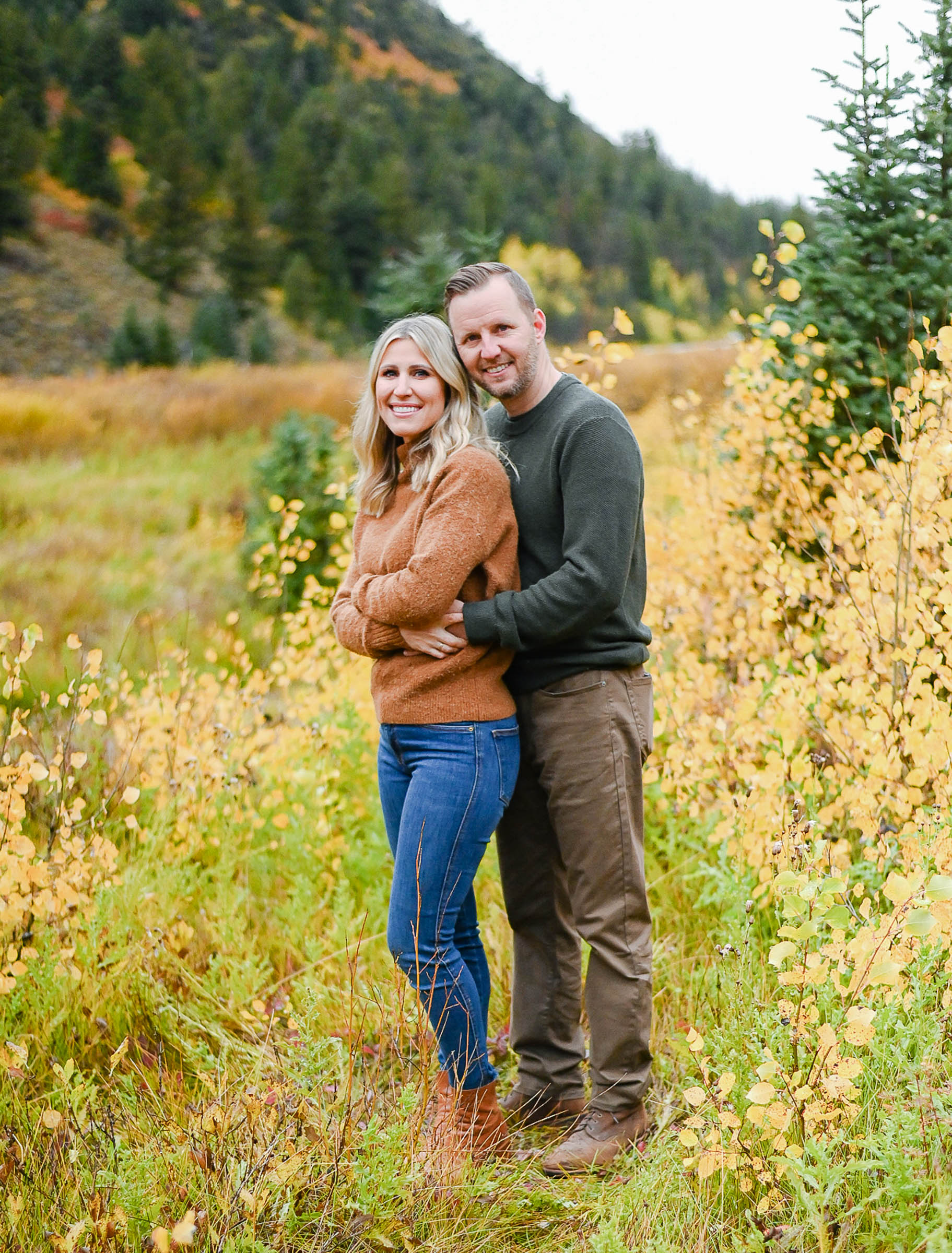 A couple embraces as they smile for the camera during the fall season in Big Cottonwood Canyon of Salt Lake City Utah. Fall family photos in Cottonwood Canyon