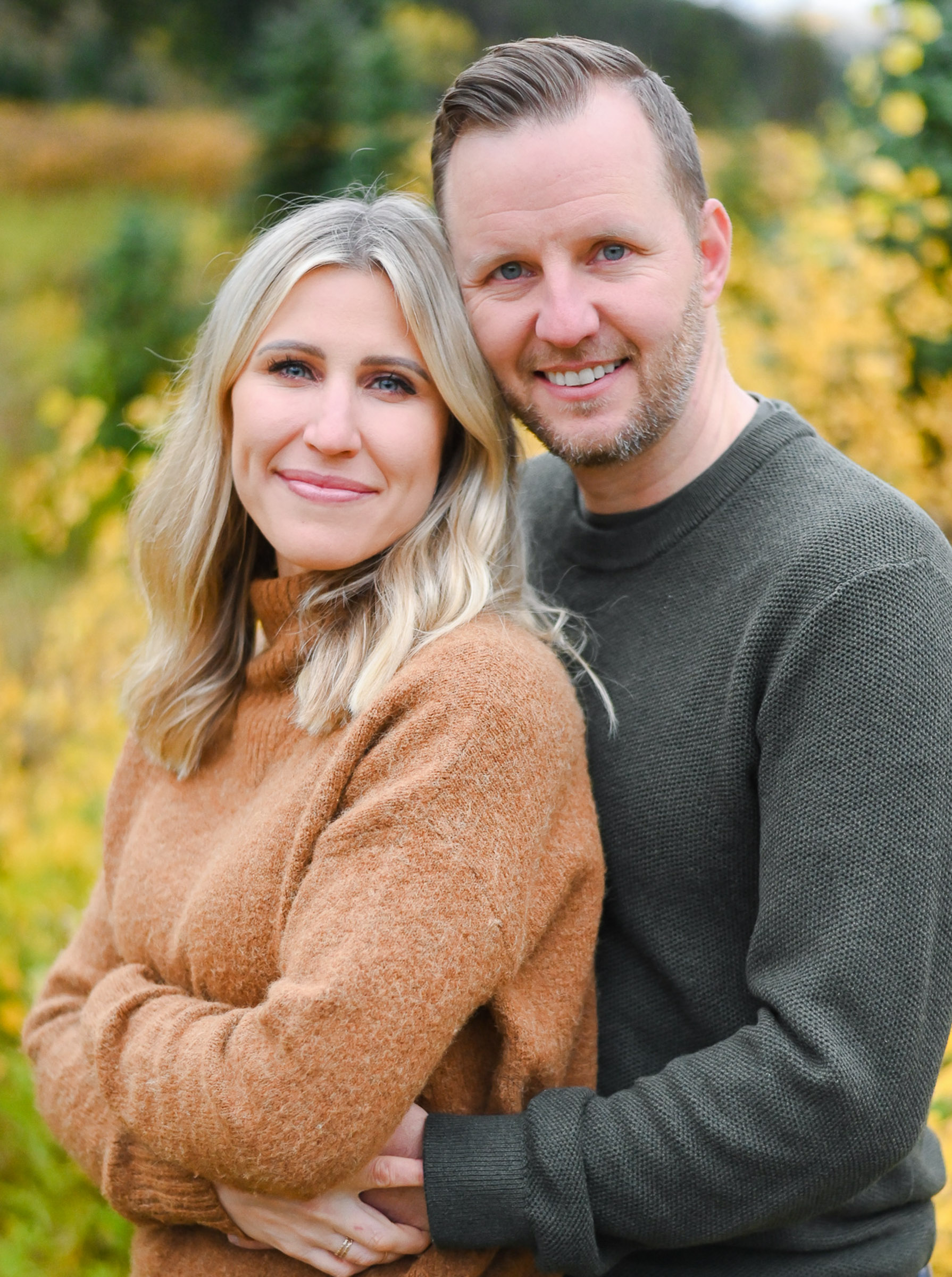A couple embraces as they smile for the camera during the fall season in Big Cottonwood Canyon of Salt Lake City Utah. Fall family photos in Cottonwood Canyon