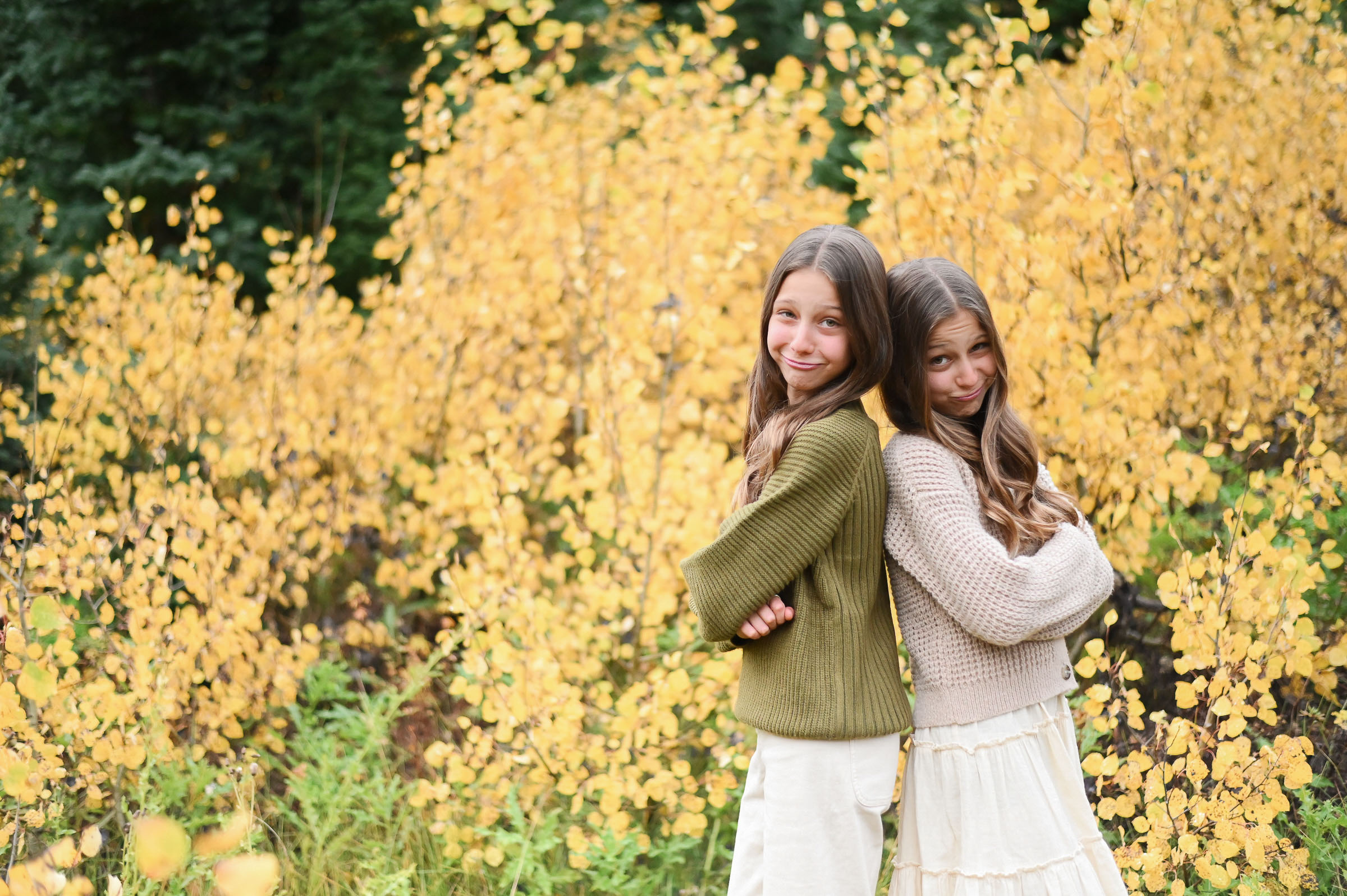 Twin girls smiling and having fun in front of the golden fall leaves of Cottonwood Canyon in Utah. Fall family photos in Cottonwood Canyon