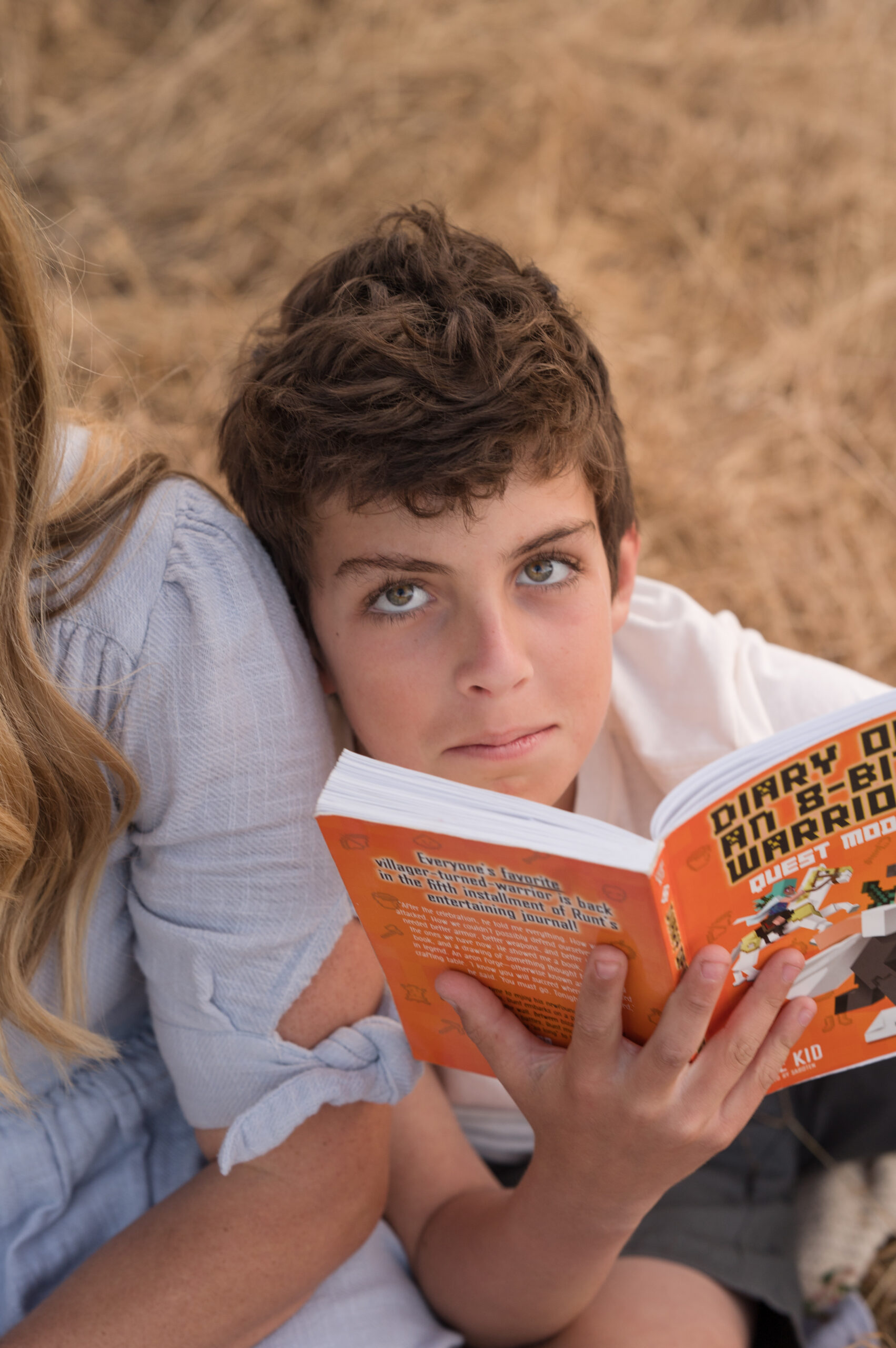 A boy looks up at the camera, taking a brake from being reading his favorite book during a candid family session at Oak Grove Park in Ripon California