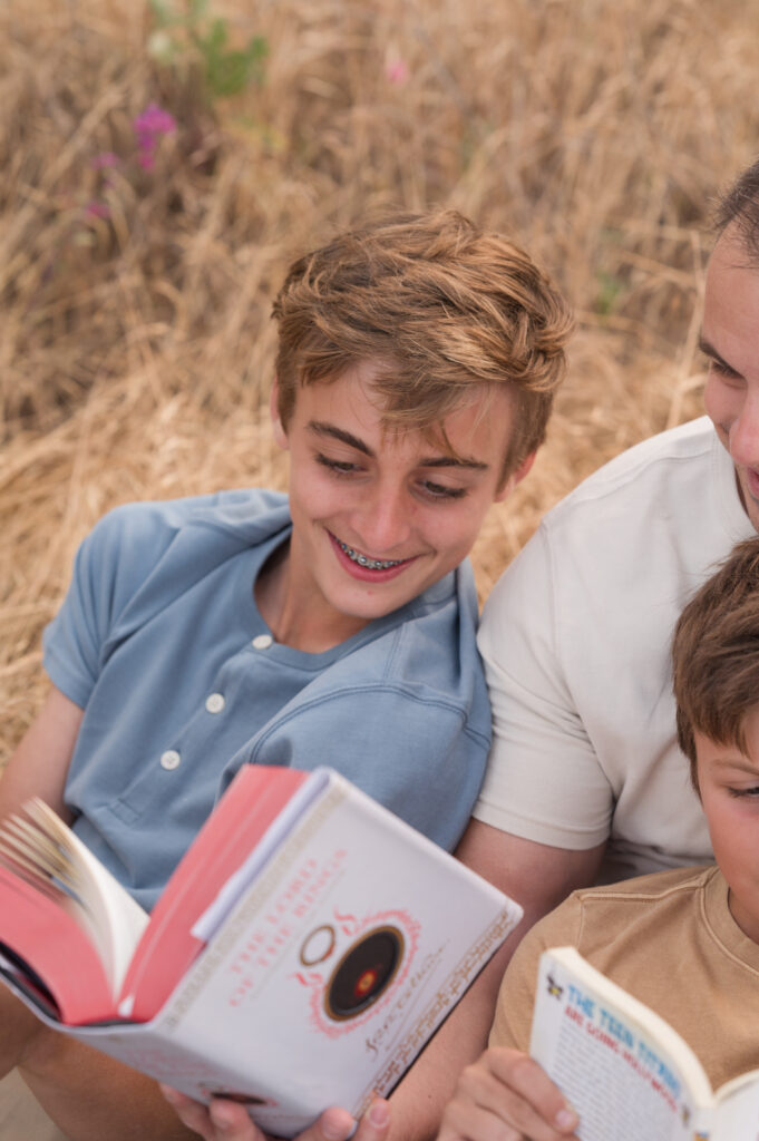 A boy smiles on at a book while he listens to his Dad read from his favorite book in Oak Grove Park in Ripon California.