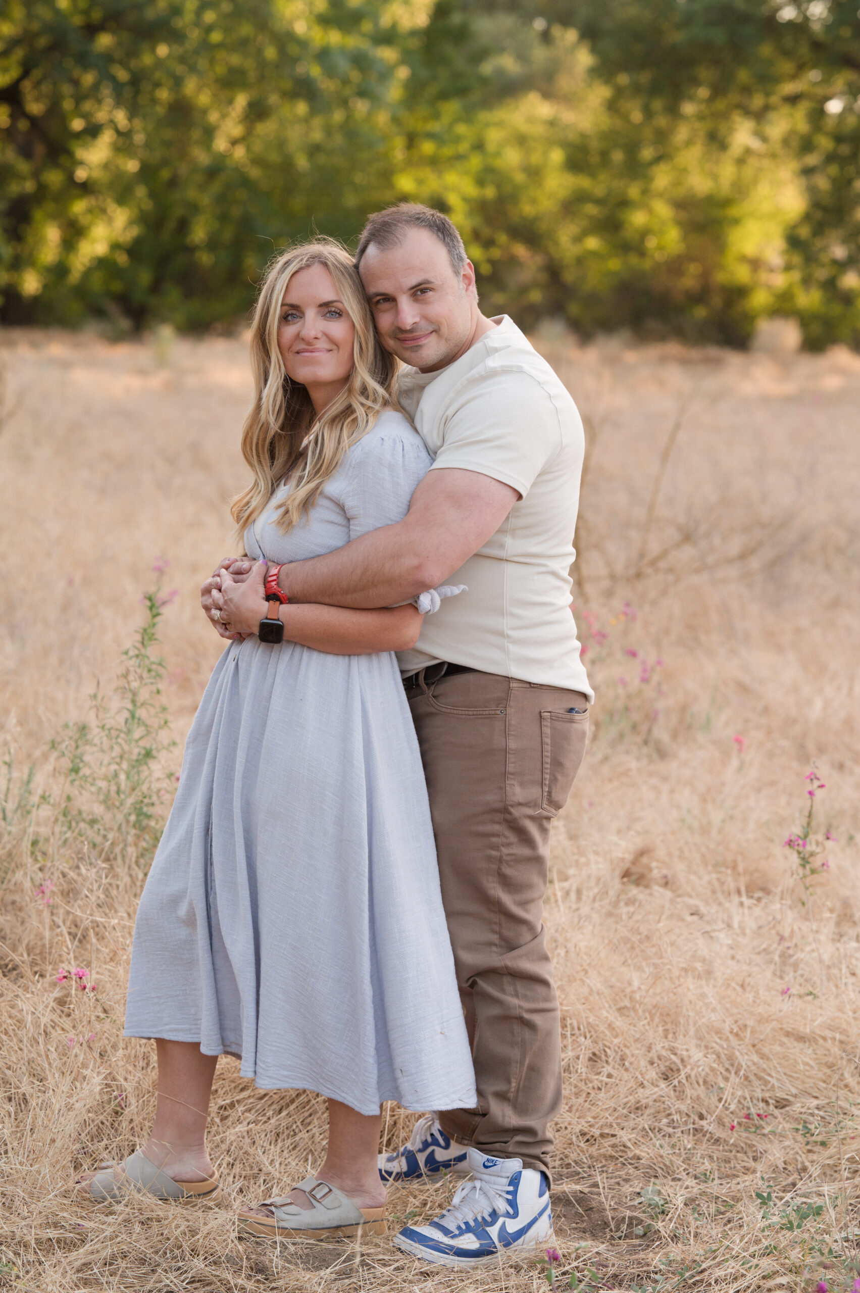 As hubby wraps his arms around his sweet heart they smile for the camera during sunset at Oak Grove Park in Ripon California.