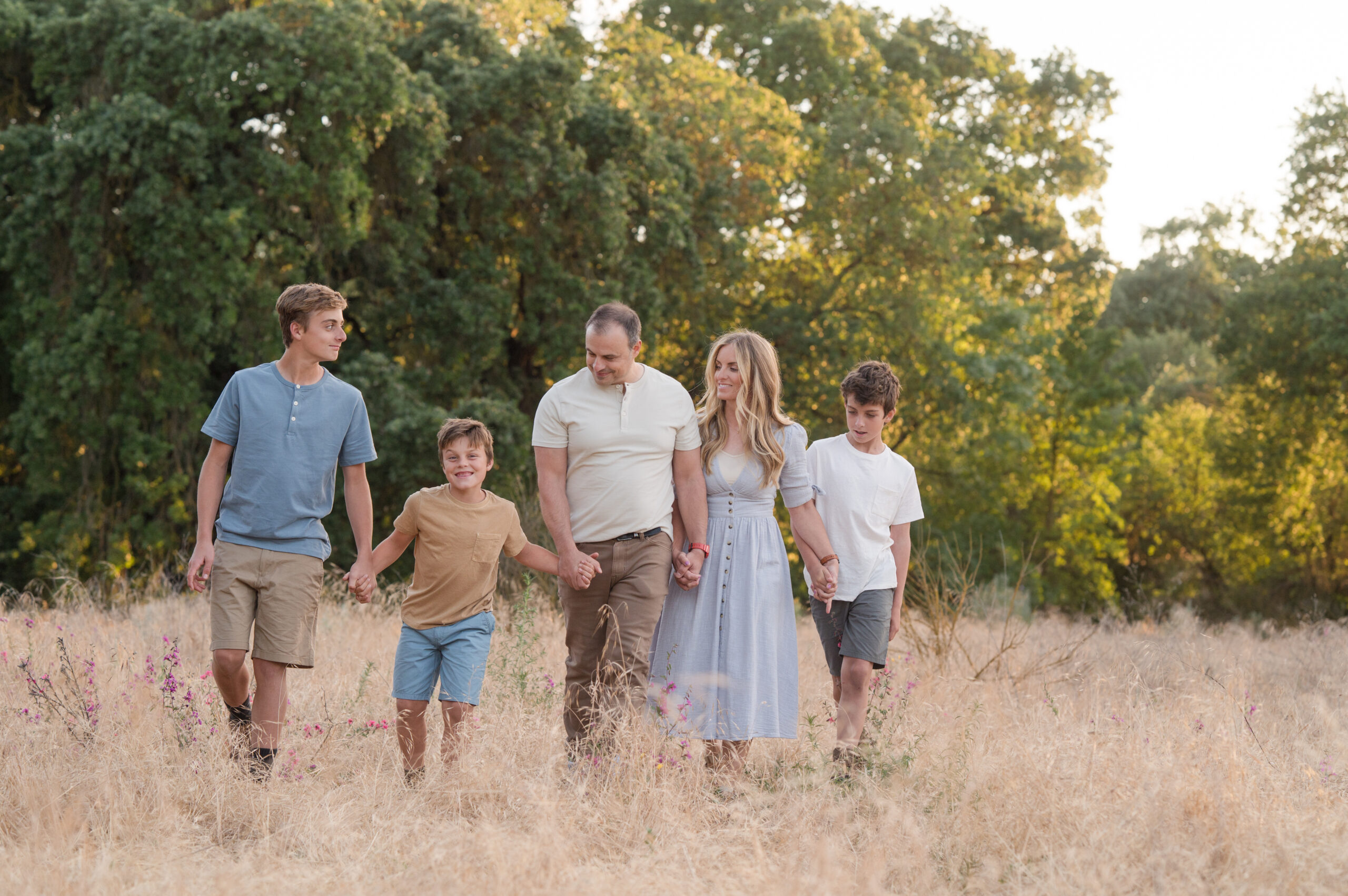 A family of five walk hand in hand as they look at one another during golden hour at Oak Grove Park in Ripon, California