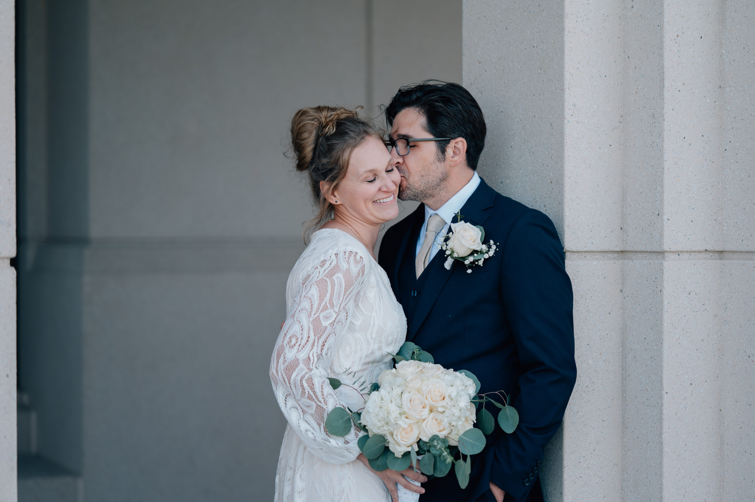 Groom snags a kiss on his bride's cheek as she closes her eyes to take it all in with a big smile on her face.