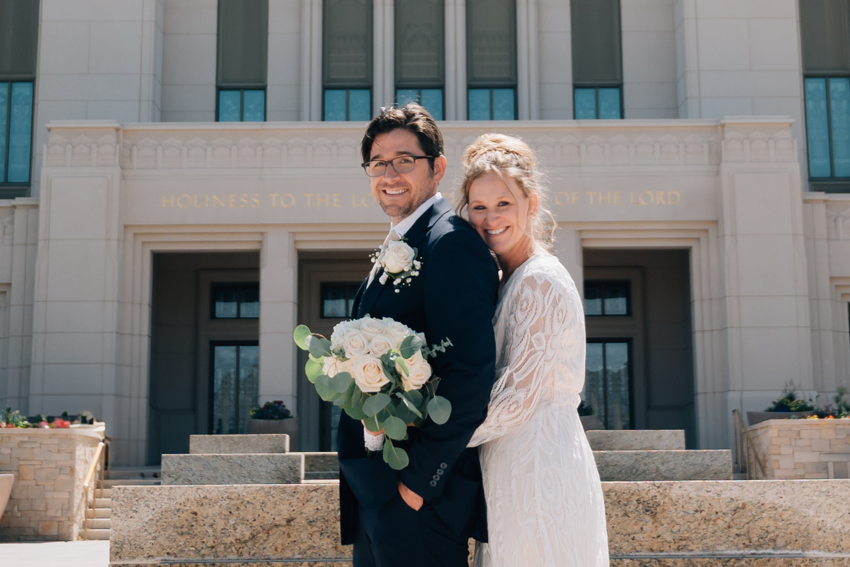 Bride and Groom smile on as they lean into one another in front of the temple in Saratoga Springs Utah