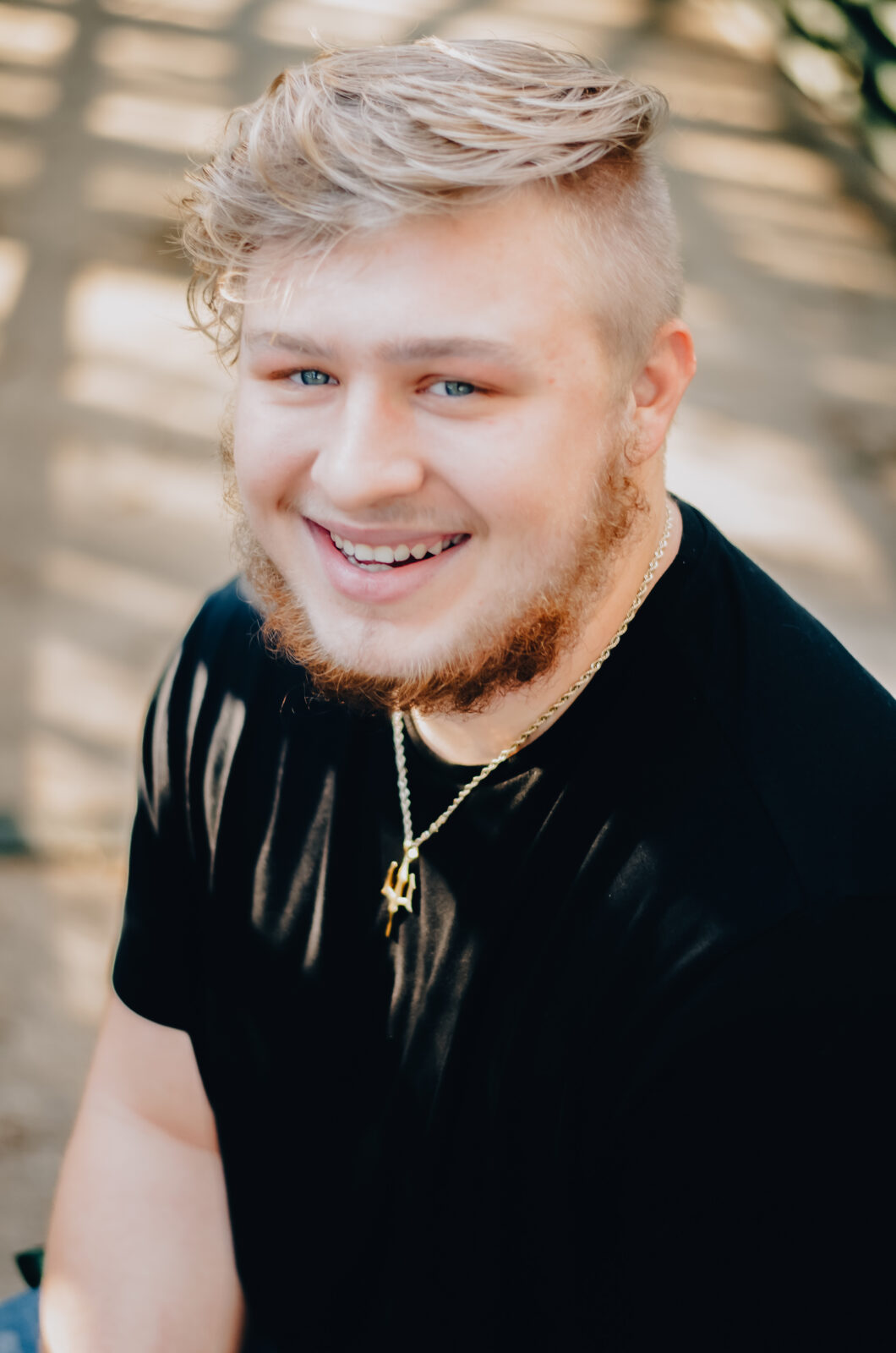 A Senior graduate smiles on the bridge for a close up while kneeling down.