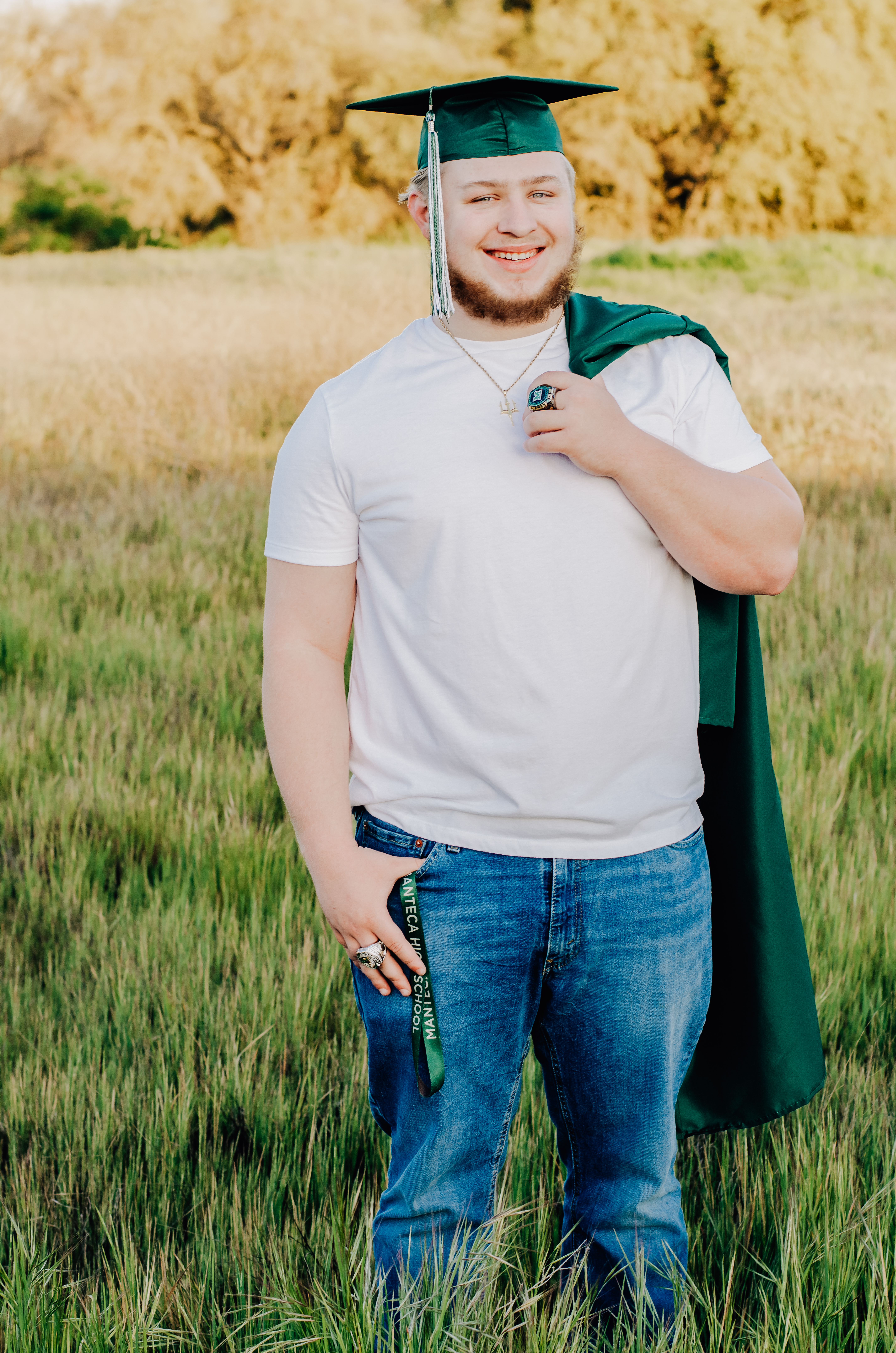 A boy in his green cap and with his gown up and over his shoulder while holding onto it with his thumb and finger. Showing off his championship rings for Manteca Buffs Football.