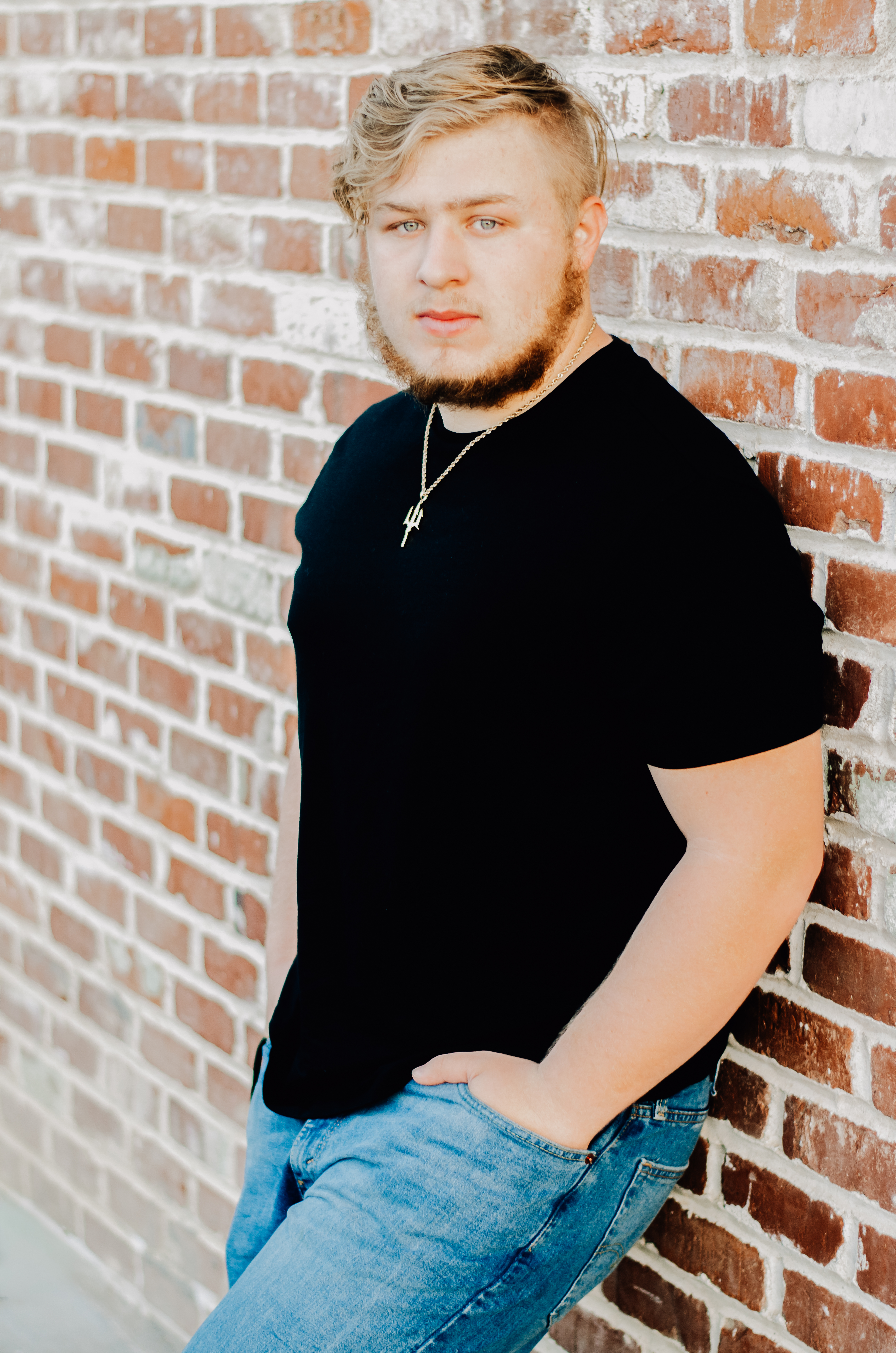 A boy leaned up against a brick wall with hands in his front pockets giving off a smoulder vibe.