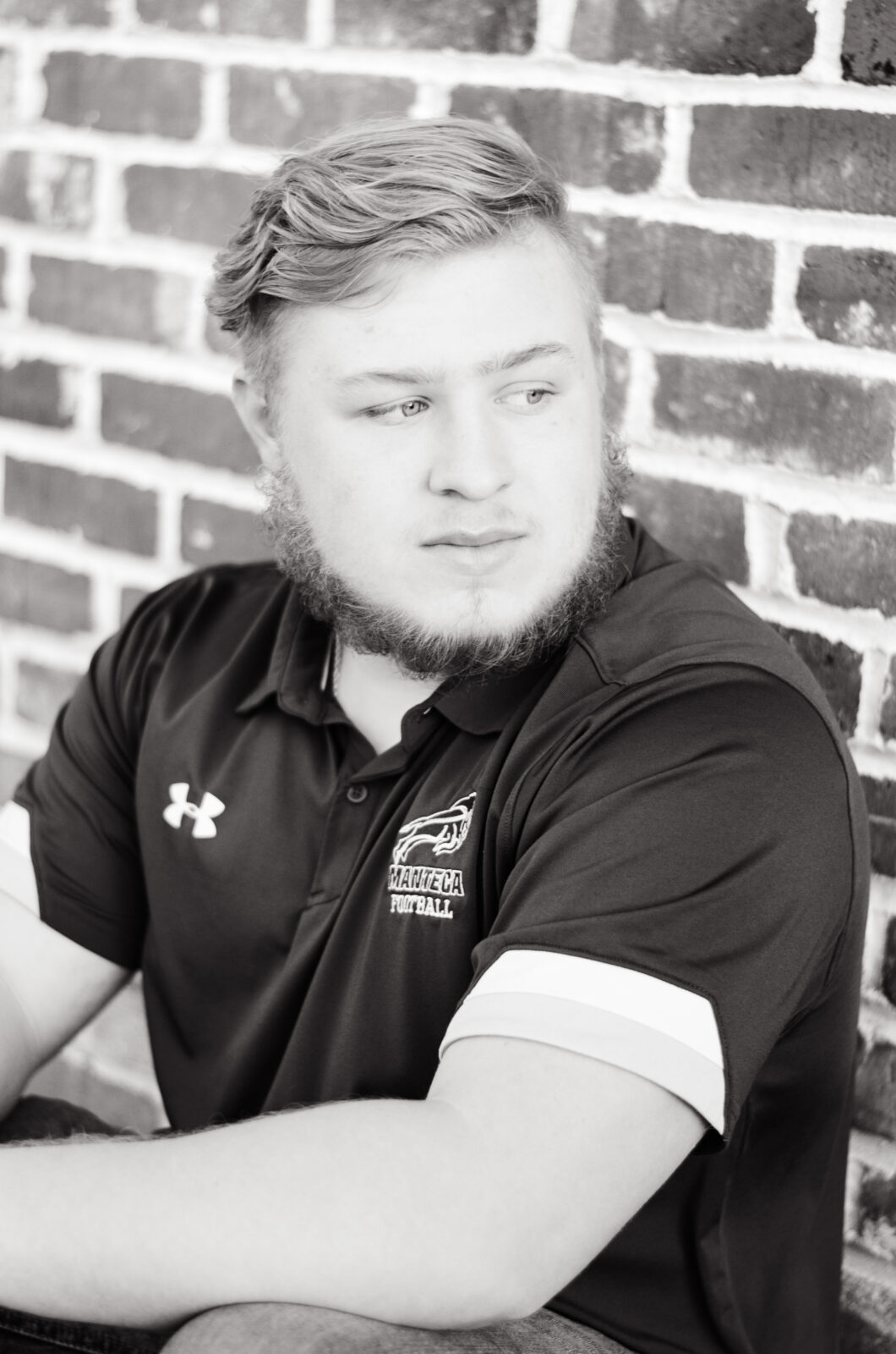 A boy sitting in front of a brick wall and leaning forward and looking to the side with hands relaxed in front of him. 