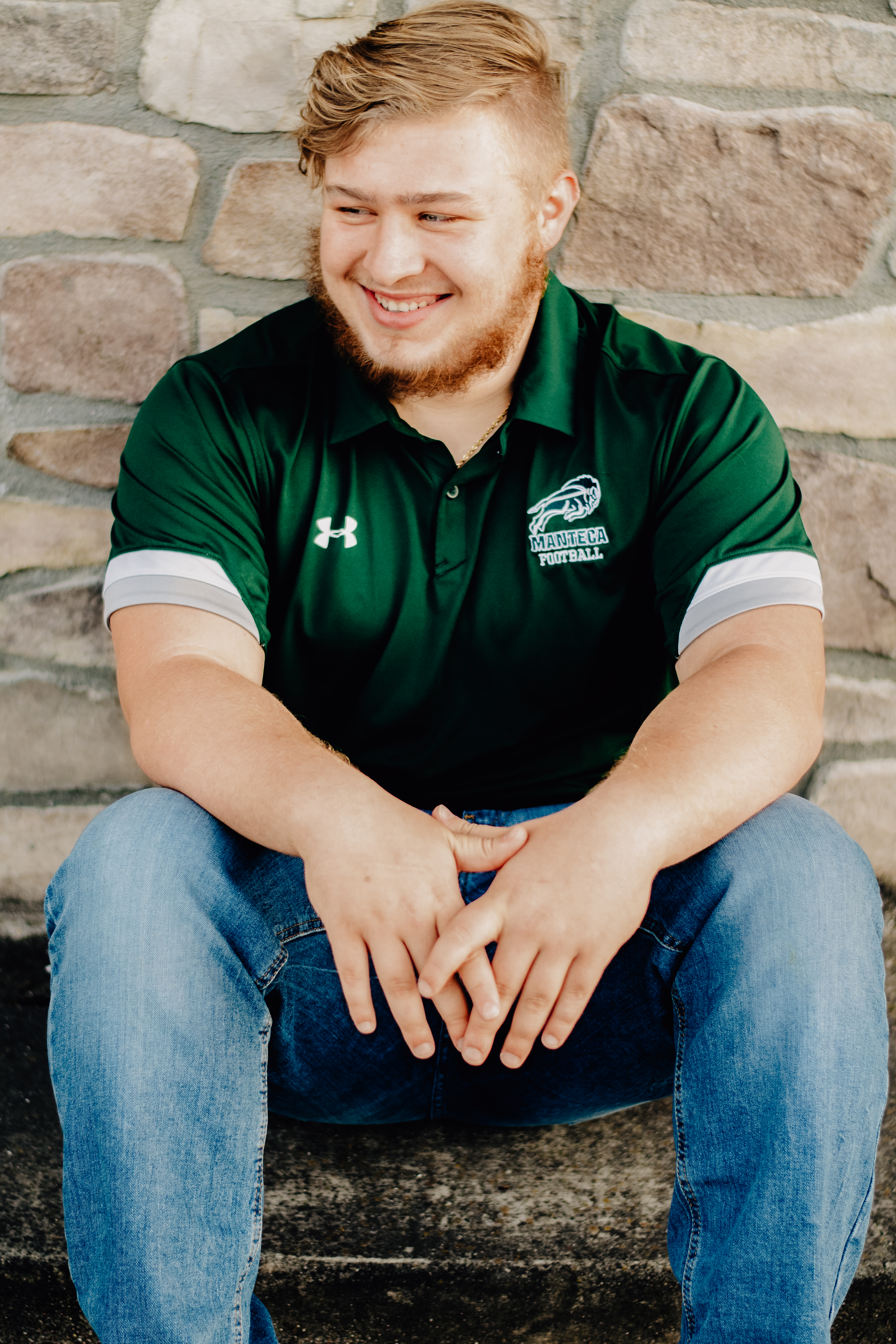A boy sitting in front of a brick wall and leaning forward with hands relaxed in front of him. 