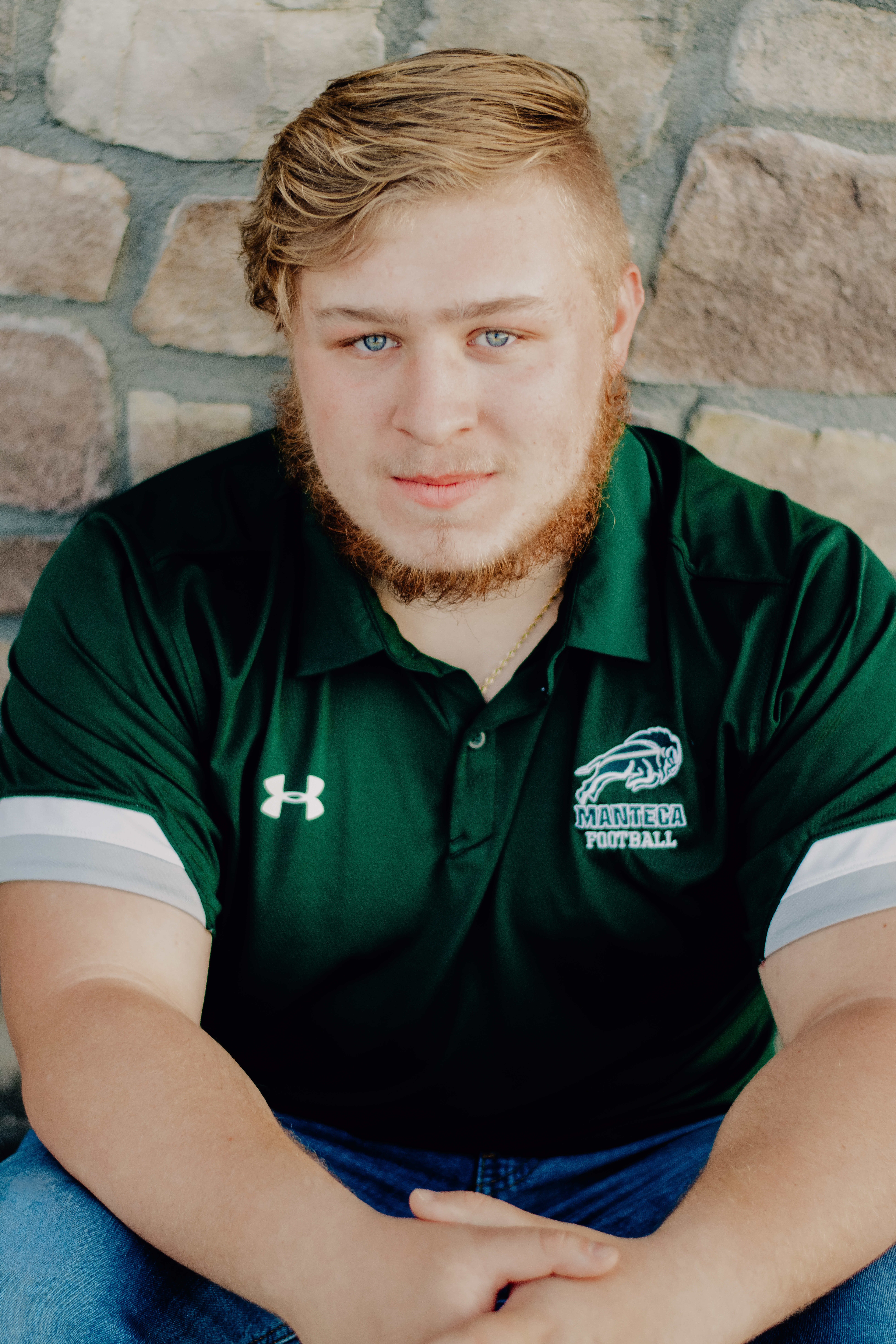 A boy sitting in front of a brick wall and leaning forward with hands relaxed in front of him. 