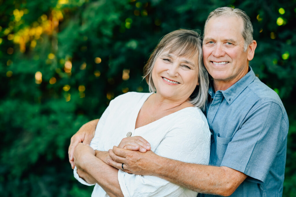 Grandpa cuddles up to Grandma from behind holding her hands.