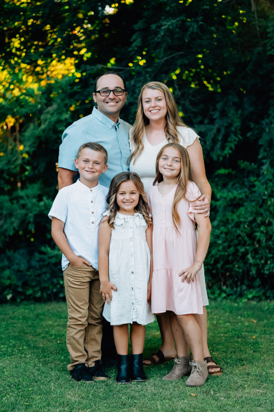 Darling family of five pose for the camera in front of a beautiful tree in the golden light hour.