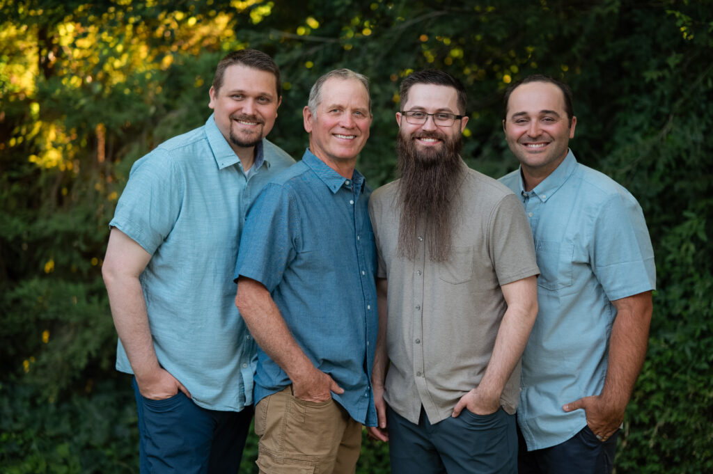 Dad with his three grown sons smiling with their hands in their pocket