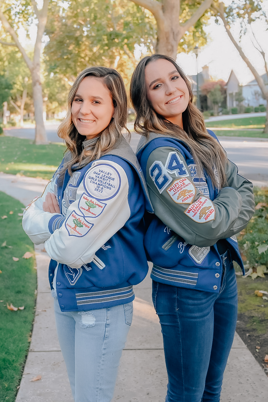 Twin girls in letterman jackets. Back to back while crossing arms in front. Both girls laughing for the camera.