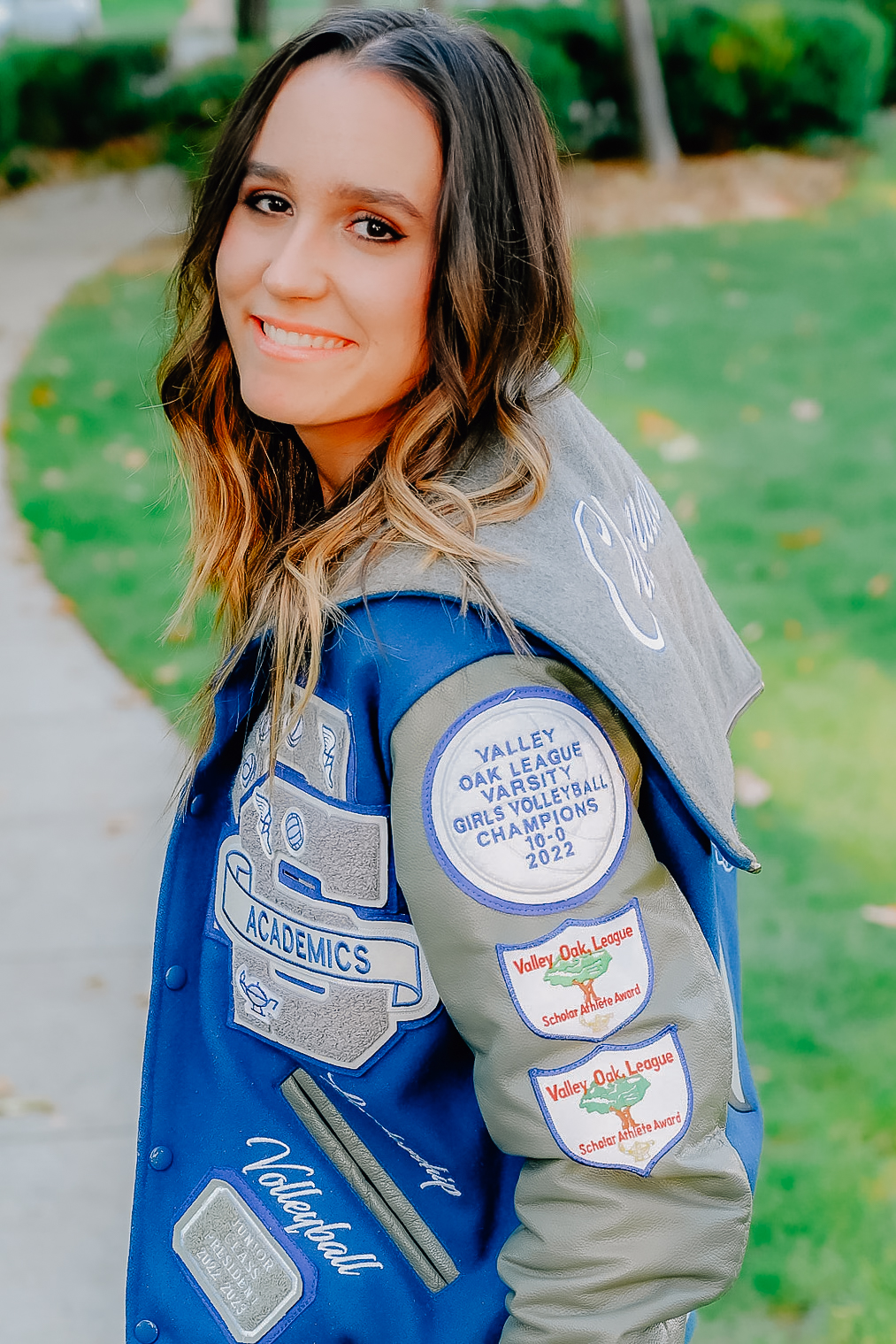 A senior girl in her letterman jacket. Looking back as she walks and smiles for the camera.