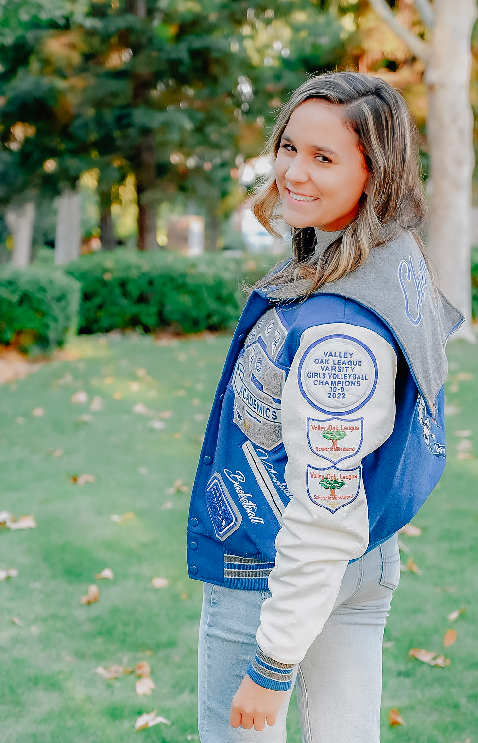 A senior girl in her letterman jacket. Looking back as she walks and smiles for the camera.
