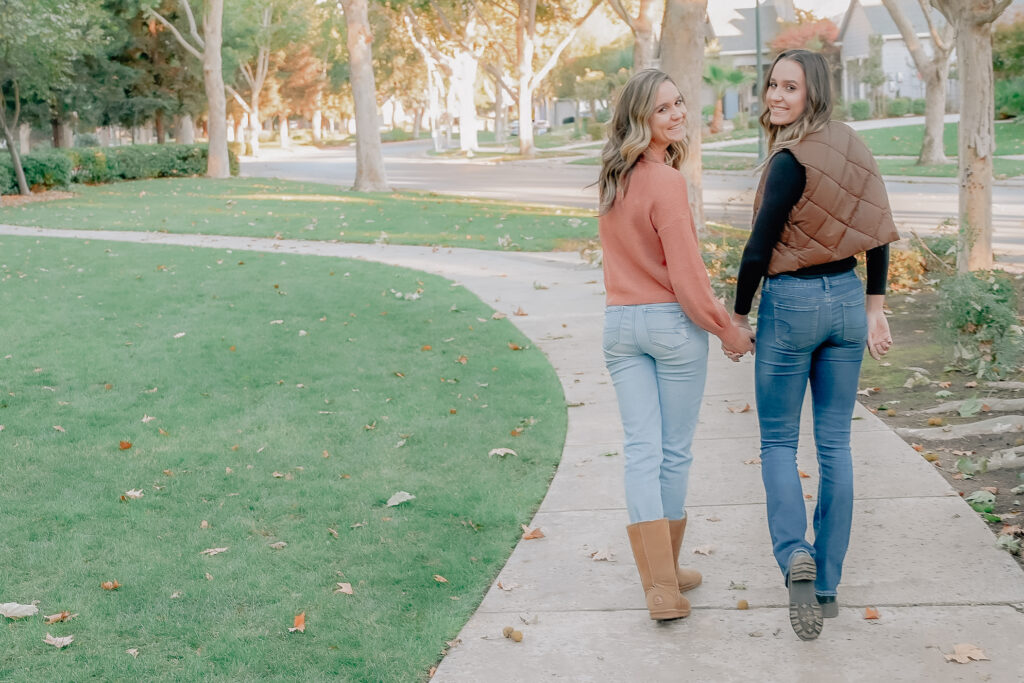 Twin Senior girls holding hands while while walking away and looking back over their shoulder on a path in a neighborhood..