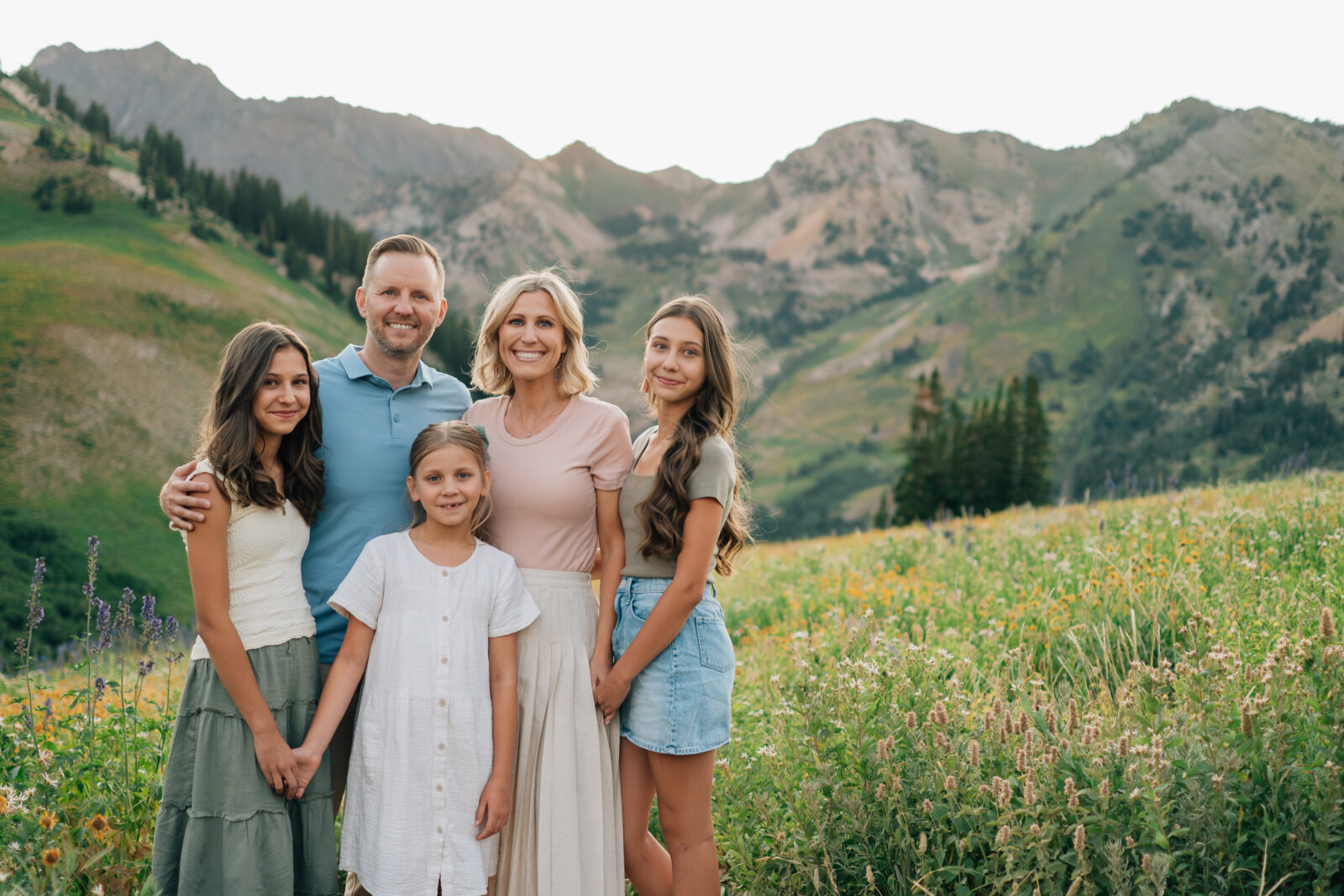A family of five smiling for the camera in front a beautiful mountain range during golden hour in Little Cottonwood Canyon, UT.