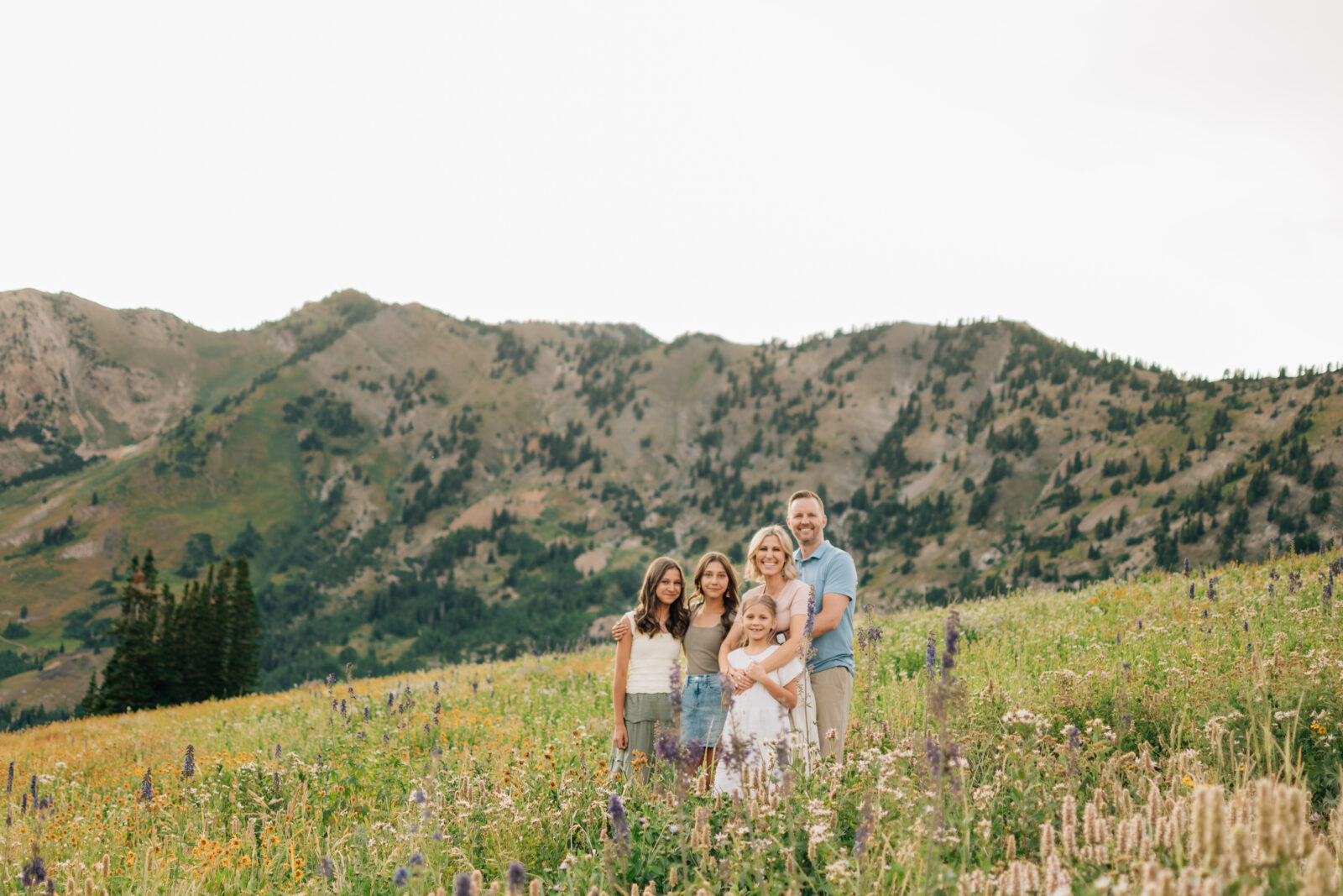 A family of five smiling for the camera in front a beautiful mountain range during golden hour in Little Cottonwood Canyon, UT. 