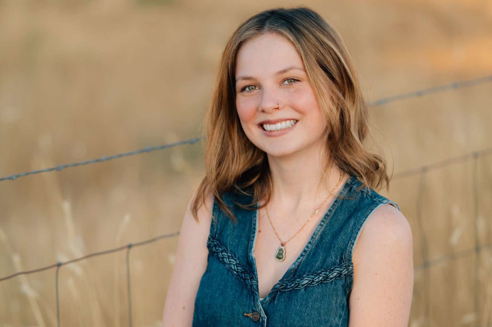 A graduating Senior poses for the camera in front of a yellow grassed field in Mapleton, UT.