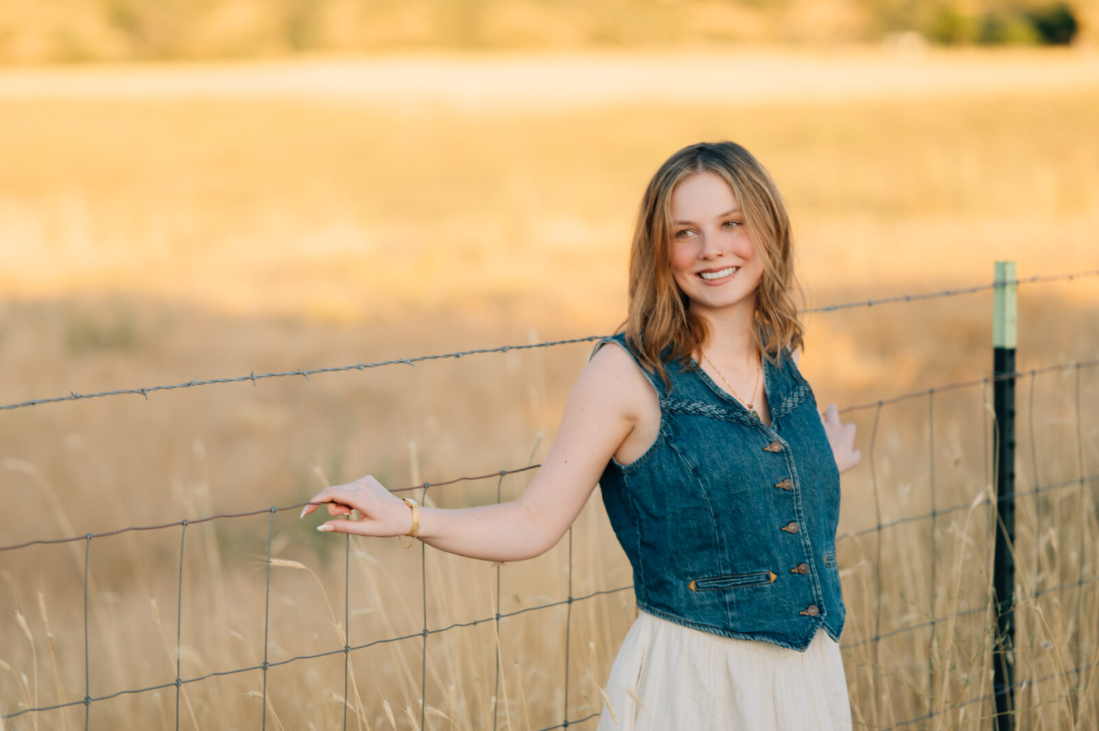 A graduating Senior poses for the camera in front of a yellow grassed field in Mapleton, UT.