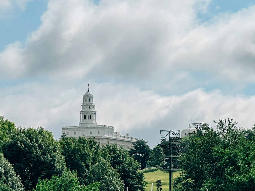 Nauvoo LDS Temple sits on a hill with greenery all in front of it and a cloud filled sky.