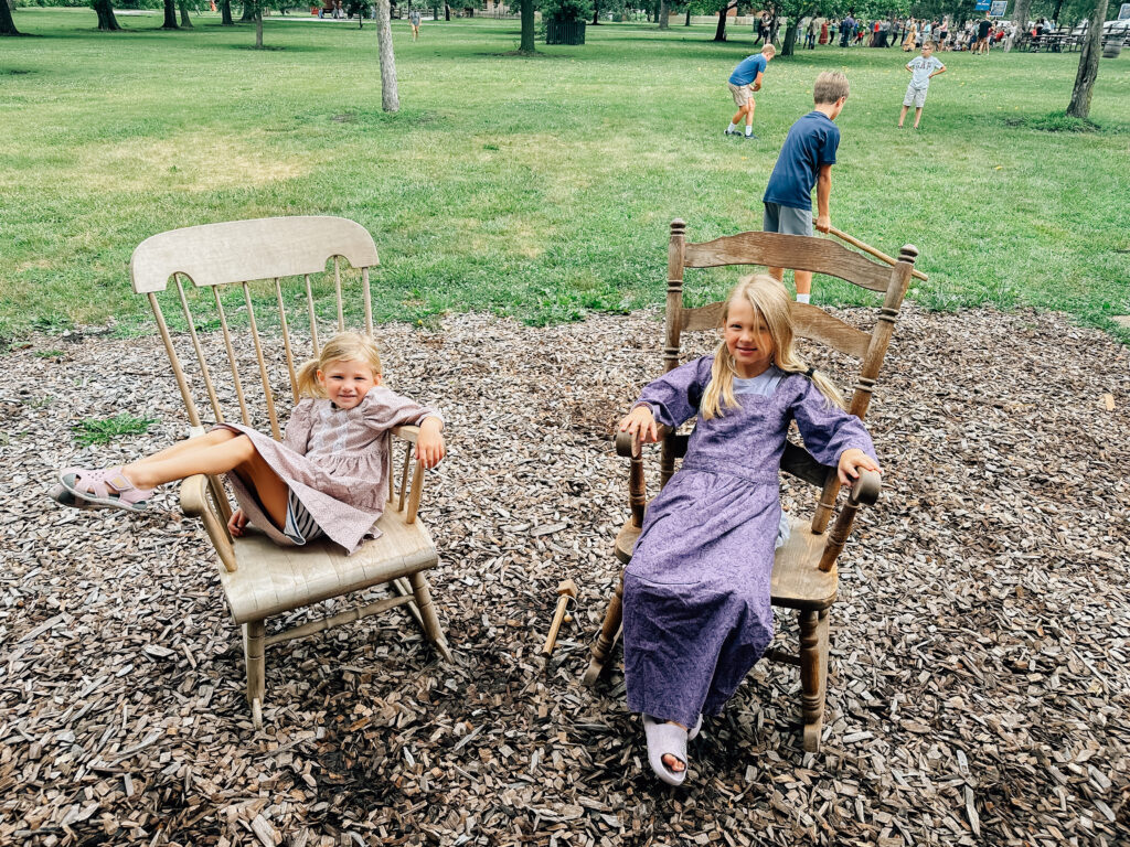 Two little girls rocking in rockers while dressed as little pioneers. 