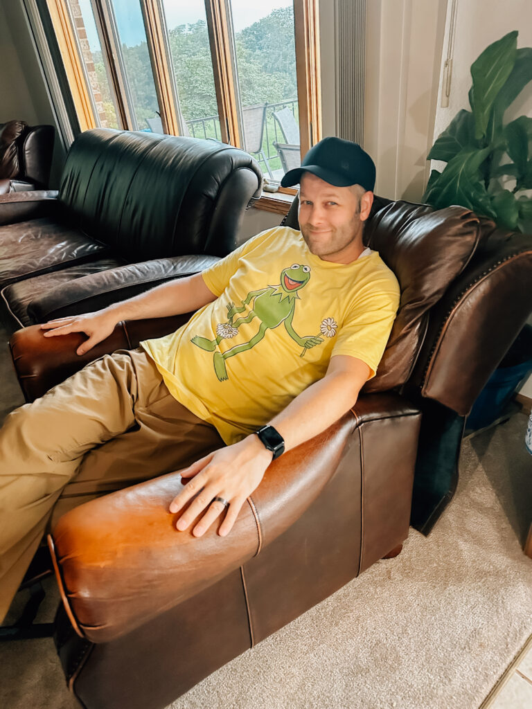 A Dad sitting on a recliner while wearing his awesome Kermit the Frog shirt taking a break. 