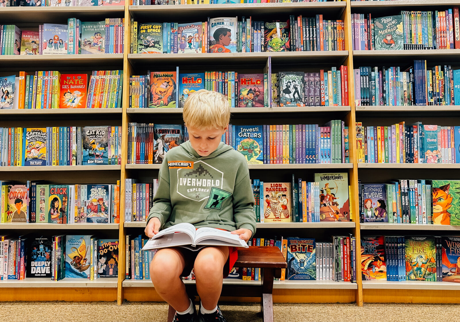A boy reading a book in front of shelves of books at Barnes and Noble in Kansas City, KS.