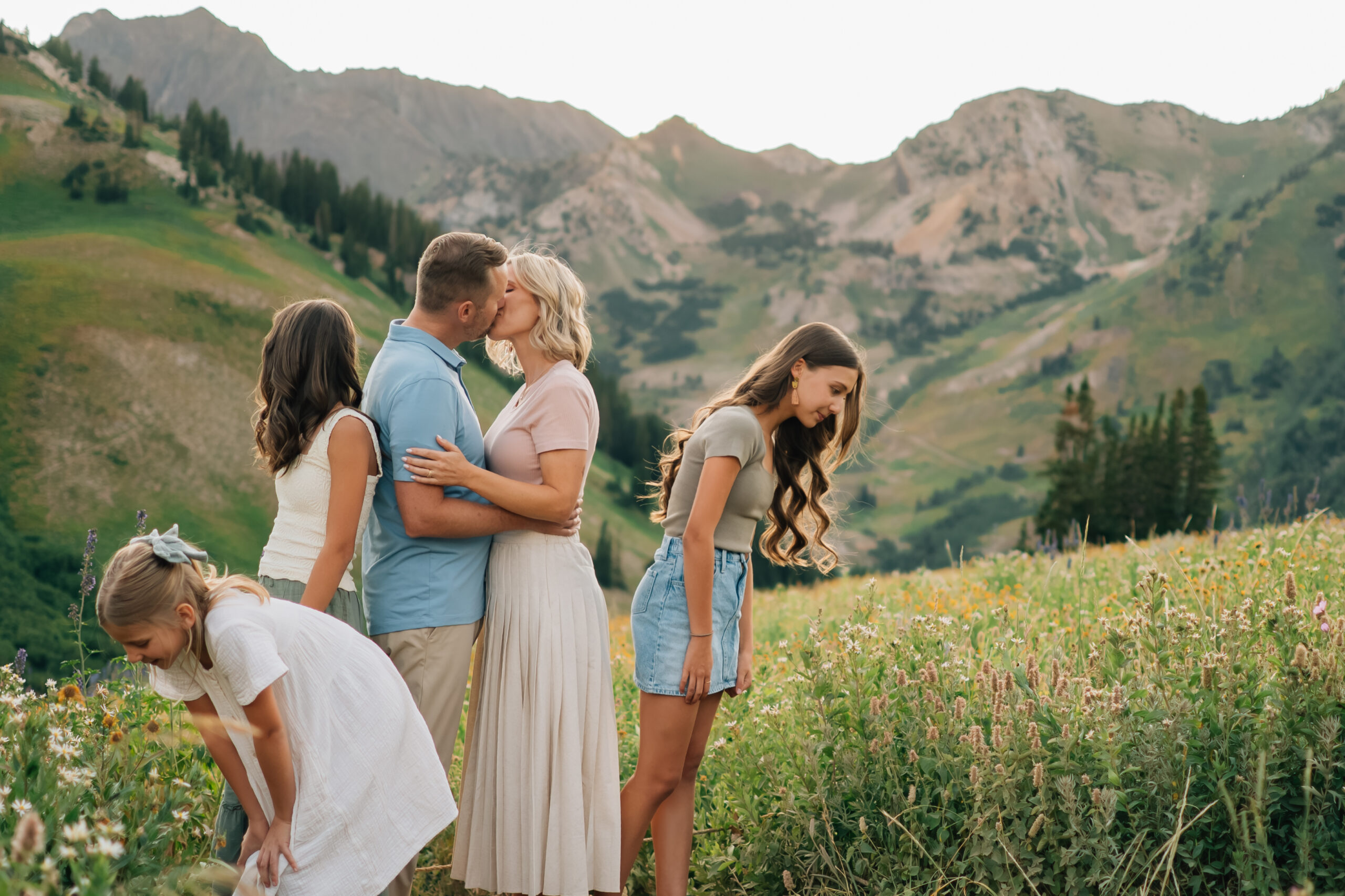 Mom & Dad kiss during a Family Session in Little Cottonwood Canyon, UT while the girls look at flowers around them.
