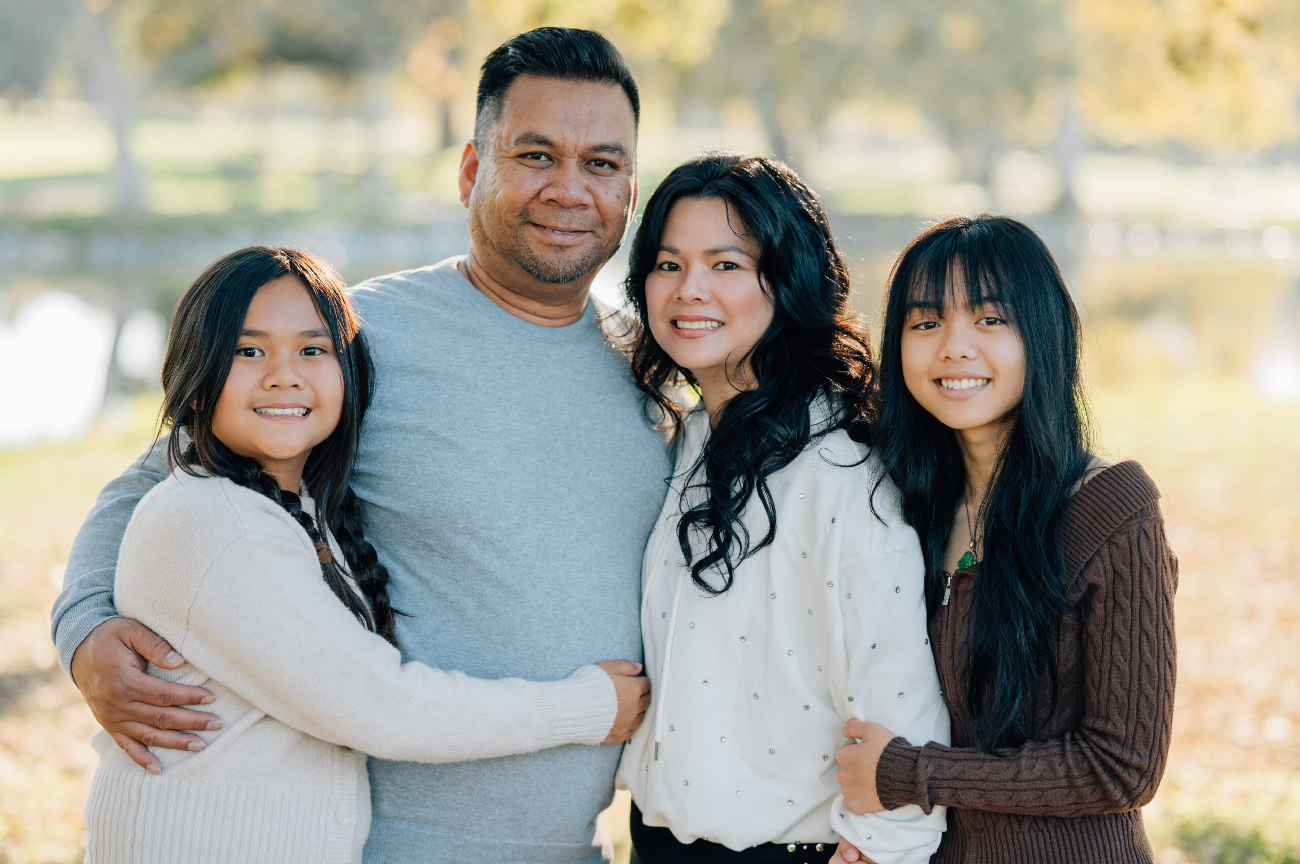 Family of four posing together by the lake at Oak Grove Park during a fall family photo session