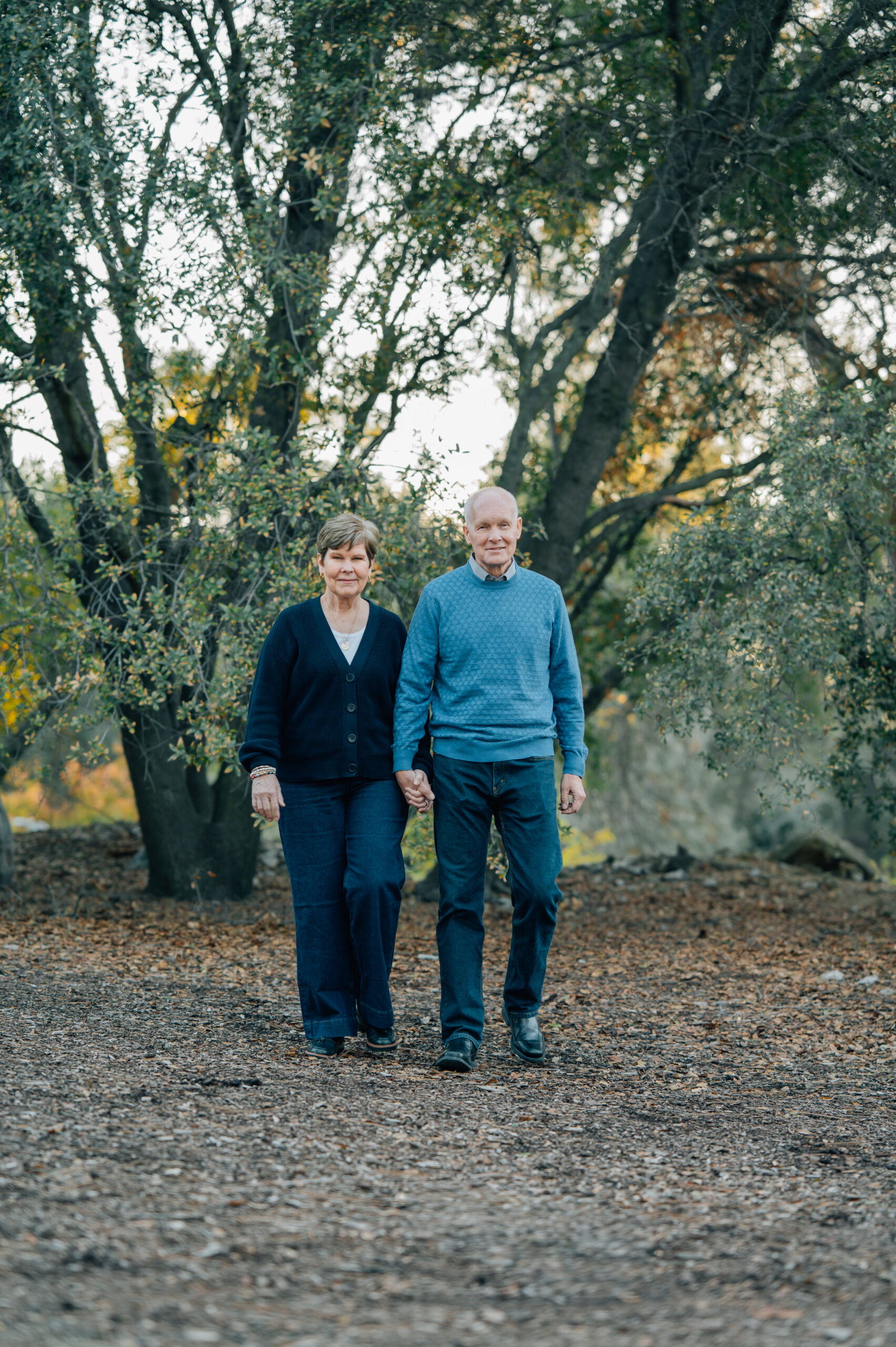 Grandparents walking hand in hand beneath oak trees during a family photo session
