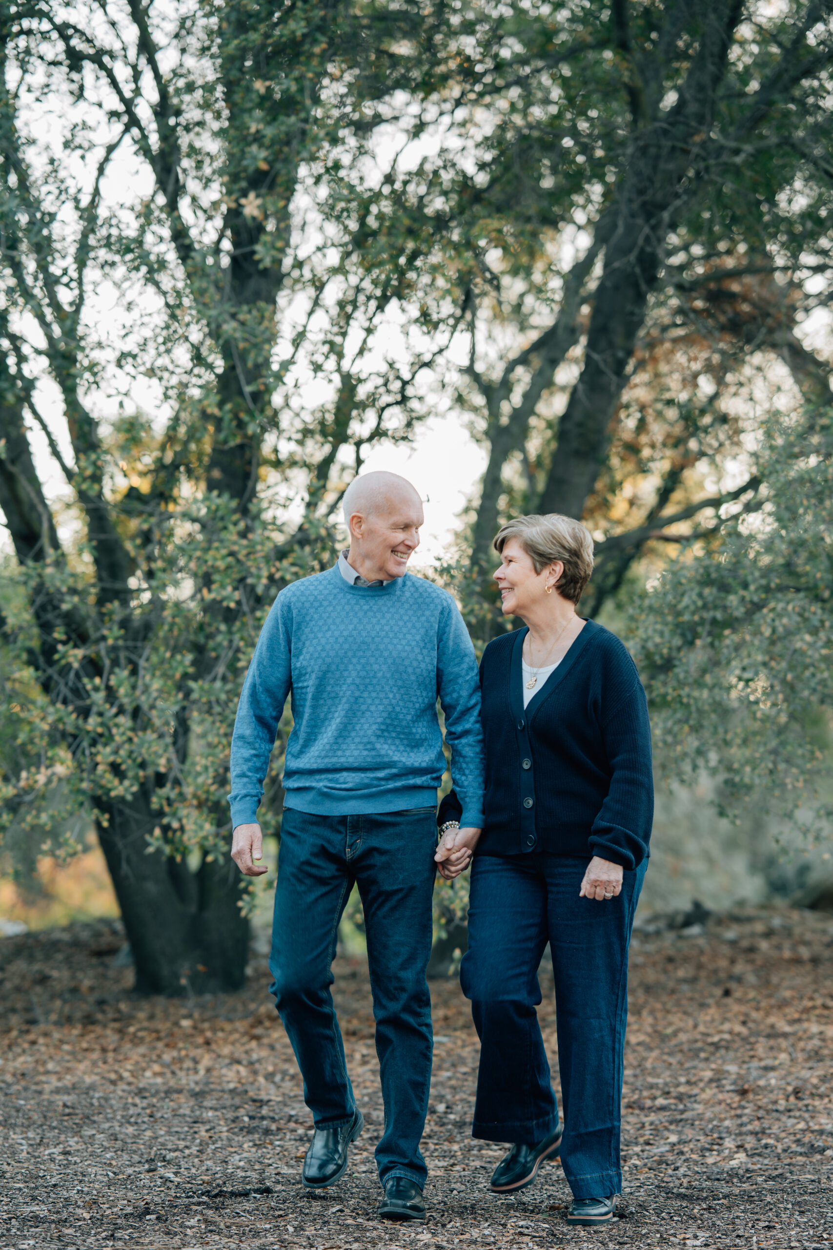 Grandparents walking hand in hand beneath oak trees during a family photo session
