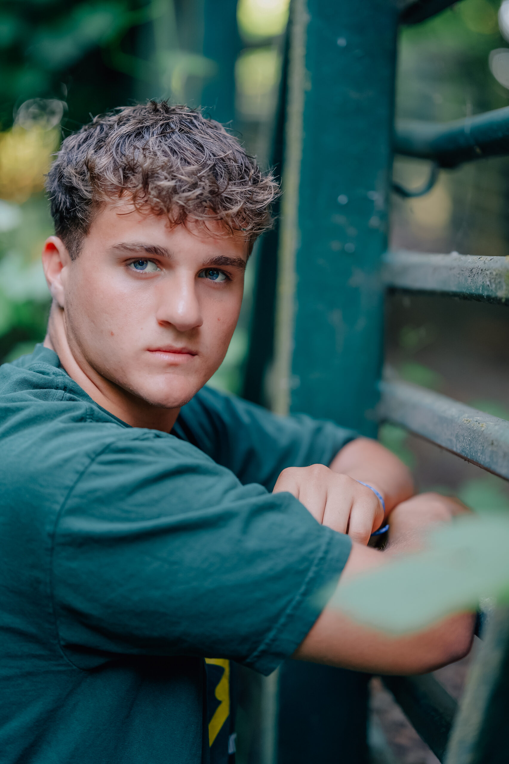 Graduate leaning against a fence with hands in pockets. 