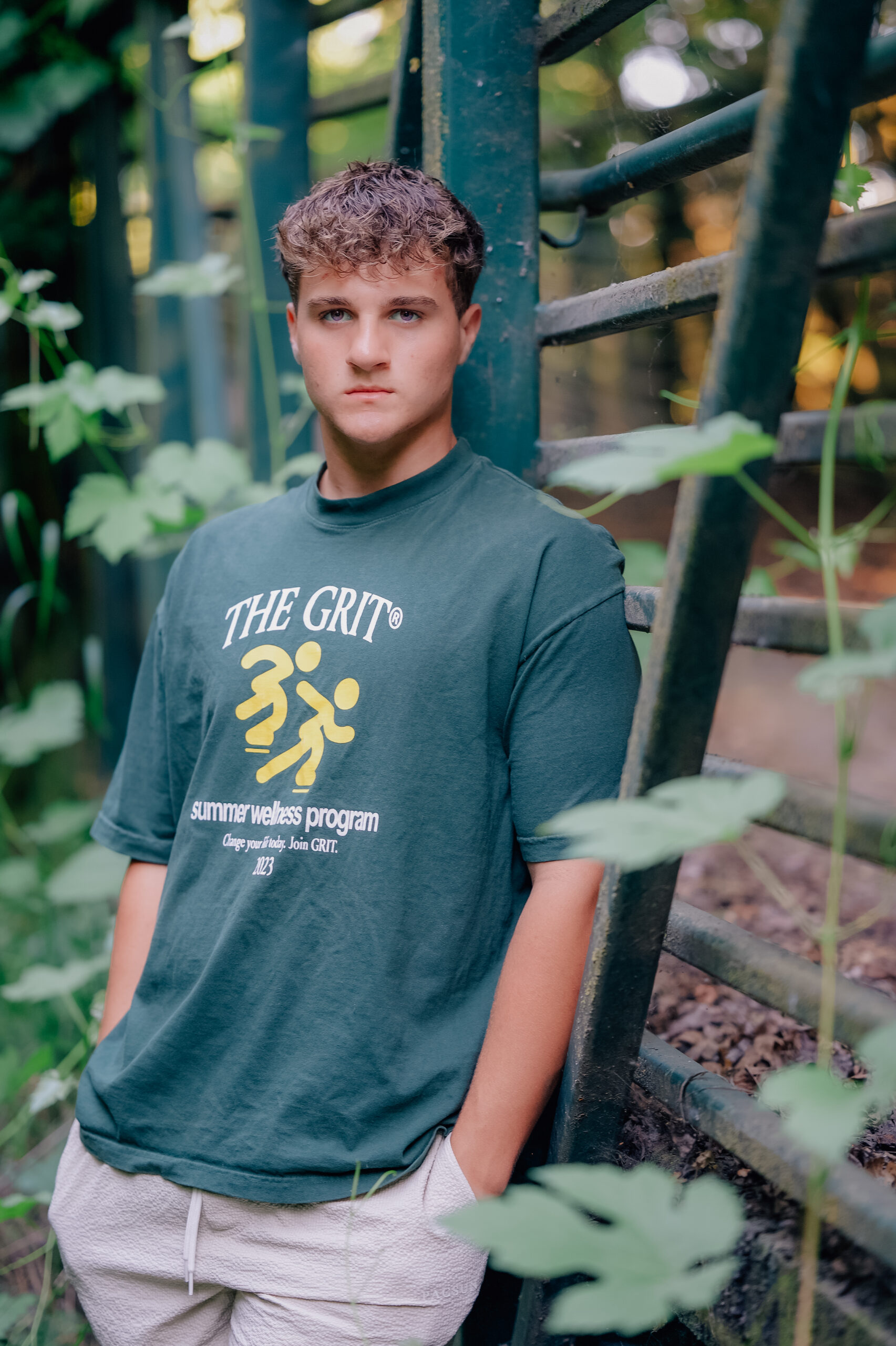 Graduate leaning against a fence with hands in pockets. 