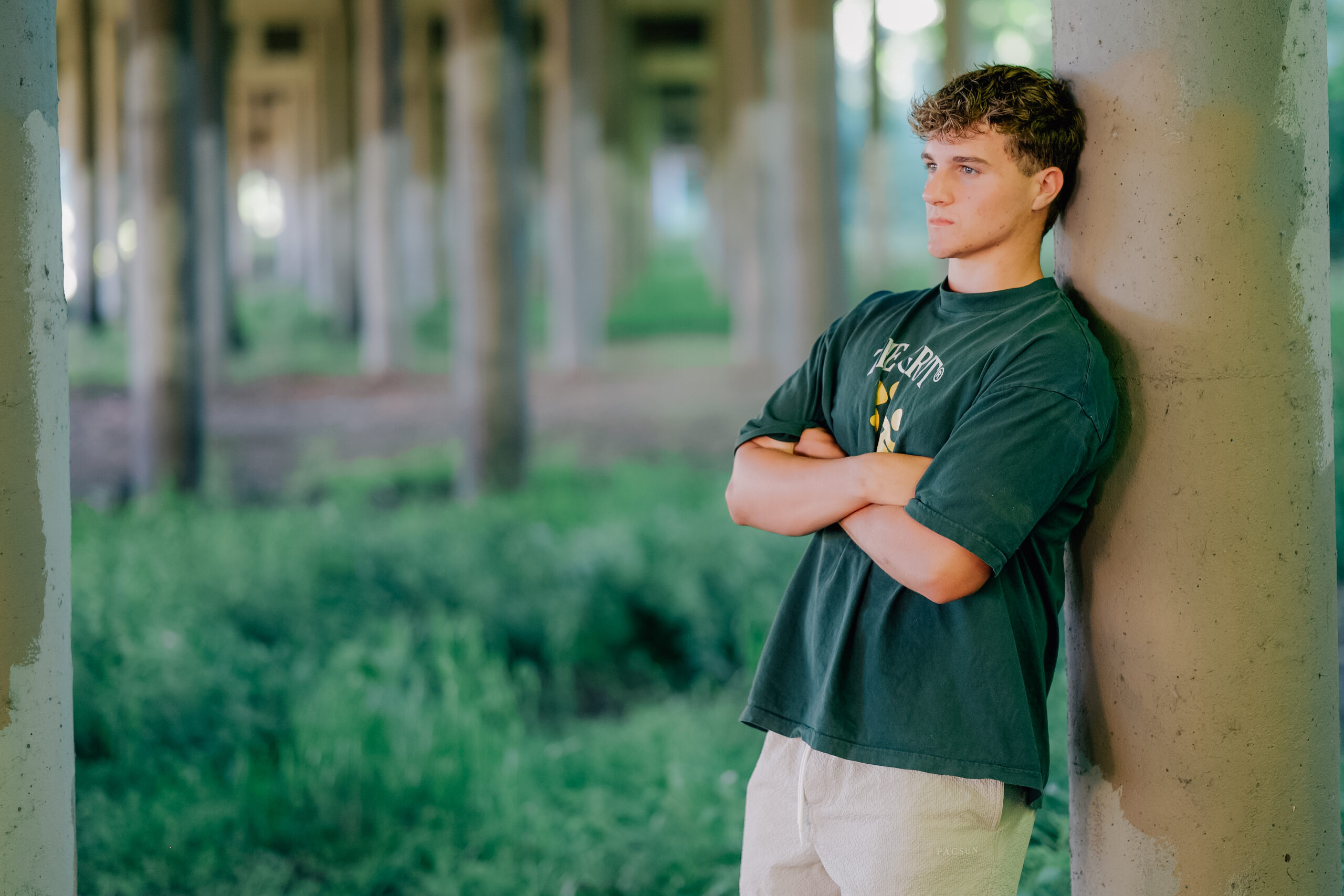 Graduate leaning against a concrete beam under an over pass.