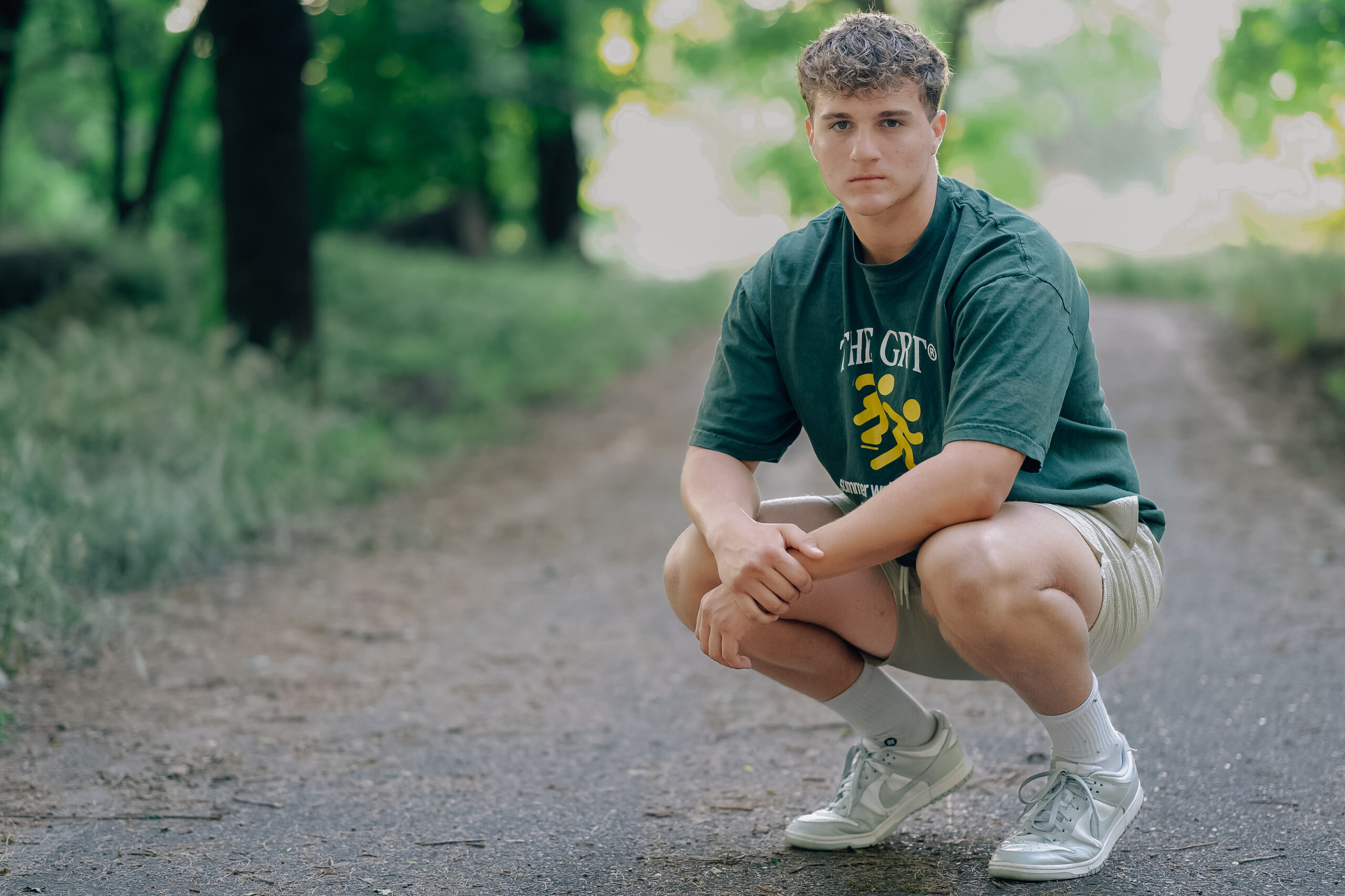 Graduate kneeling in a players stance on a path in a park.