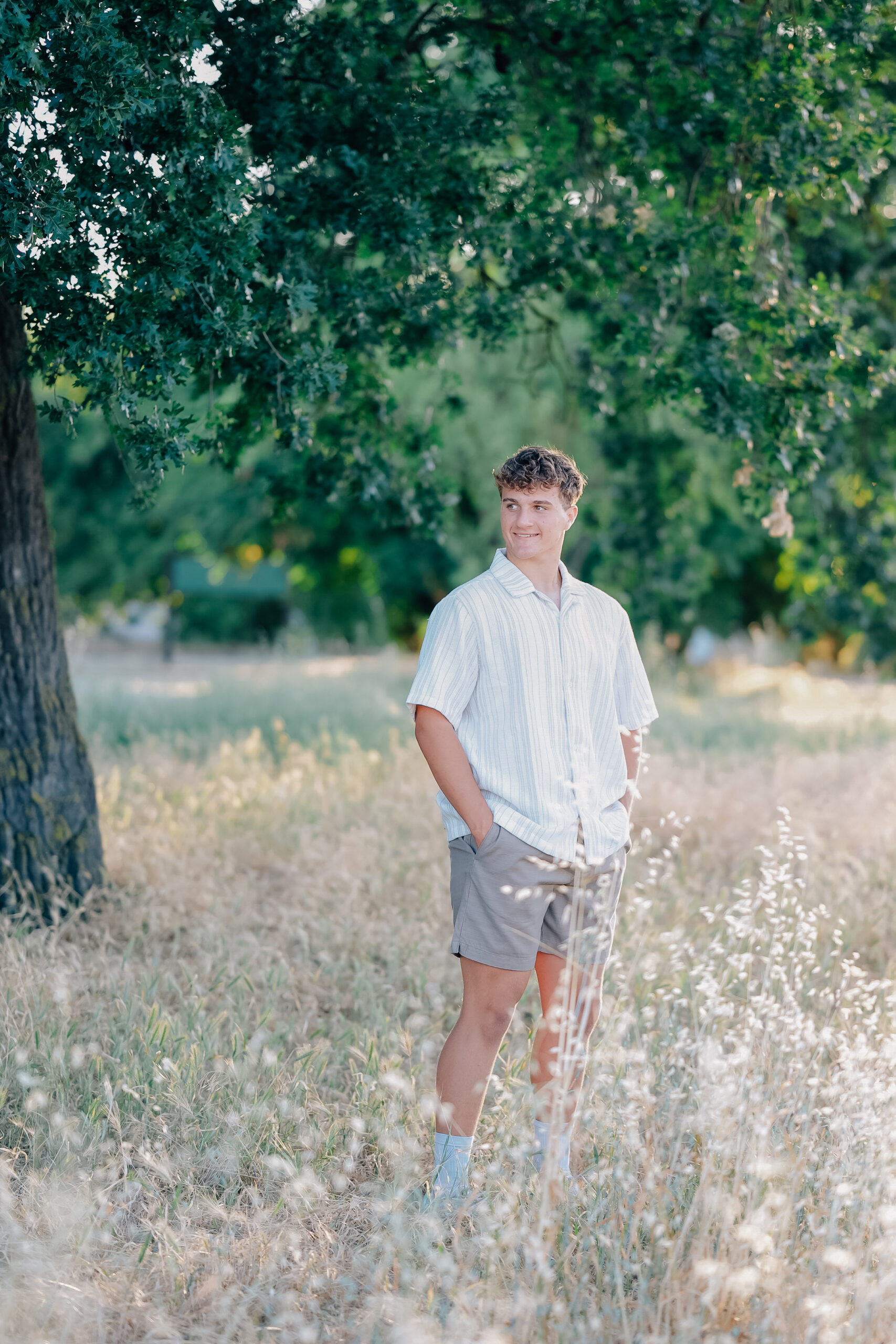 Graduate standing strong with hands in pockets while looking to the side and smiling. 