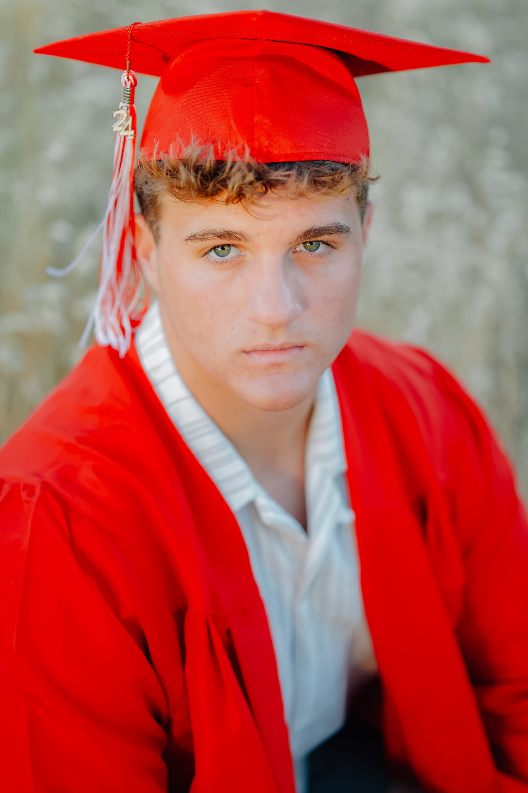 Graduate sitting in a field of tall golden grass dressed in his graduation robes during a sunset shoot.
