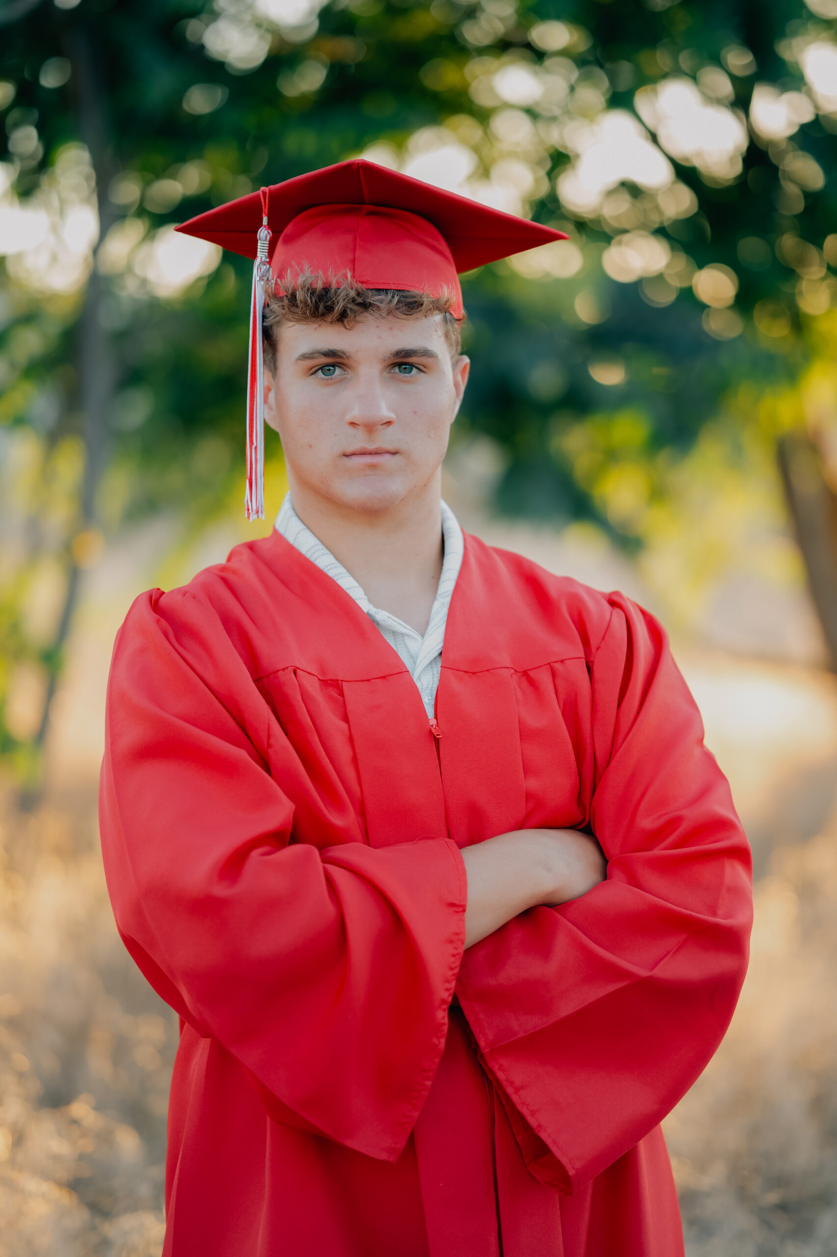 Graduate standing with his crossed in a field of tall golden grass dressed in his graduation robes during a sunset shoot.